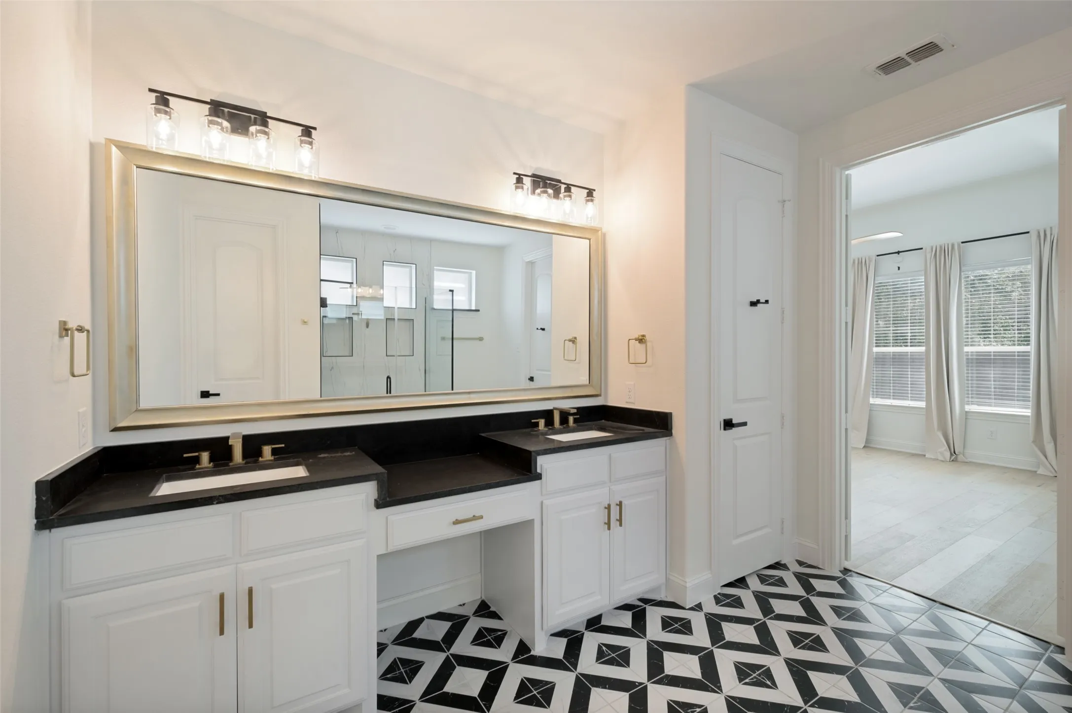 Dual vanity with dark countertops, white cabinetry, and a large framed mirror
