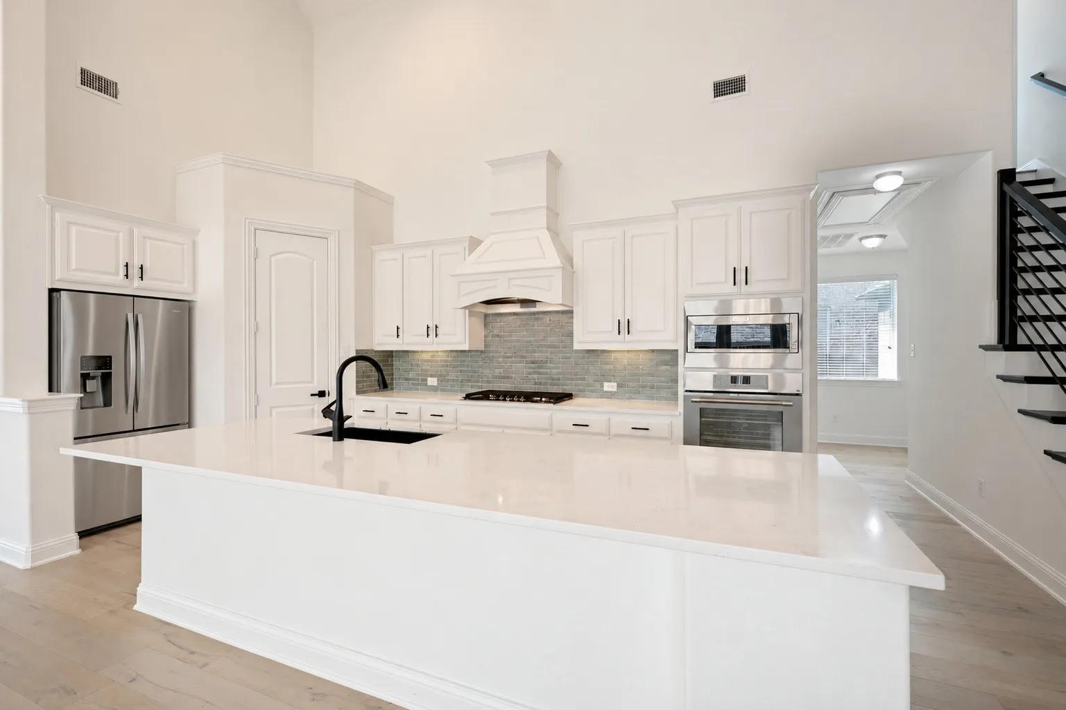 Expansive kitchen with a large island, white cabinetry, integrated stainless steel appliances, a tile backsplash, and wood-finish flooring