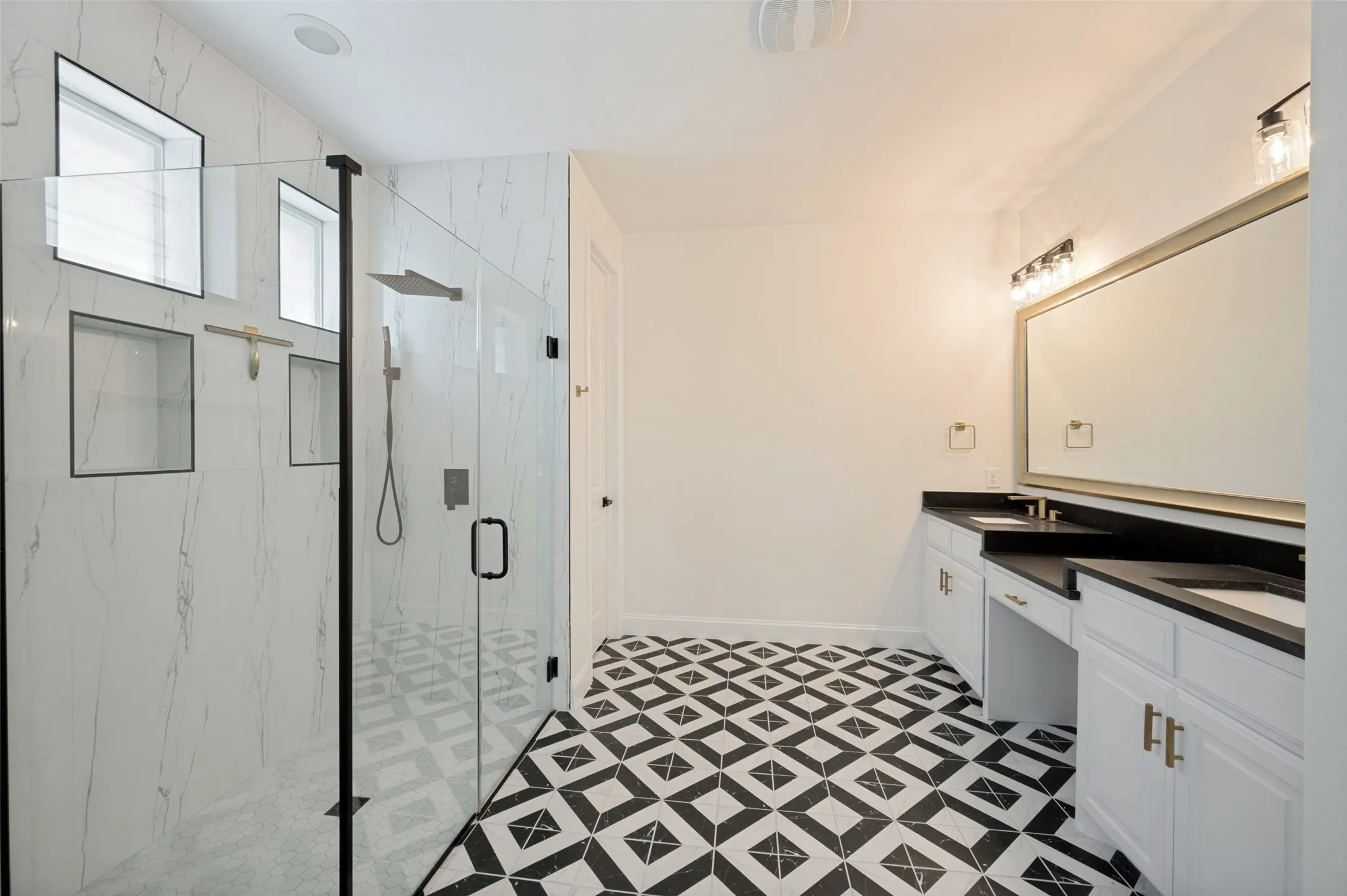 Walk-in shower with full-height tile surround and glass enclosure, dual vanity with undermount sinks and dark countertops, decorative floor tiling, and recessed lighting