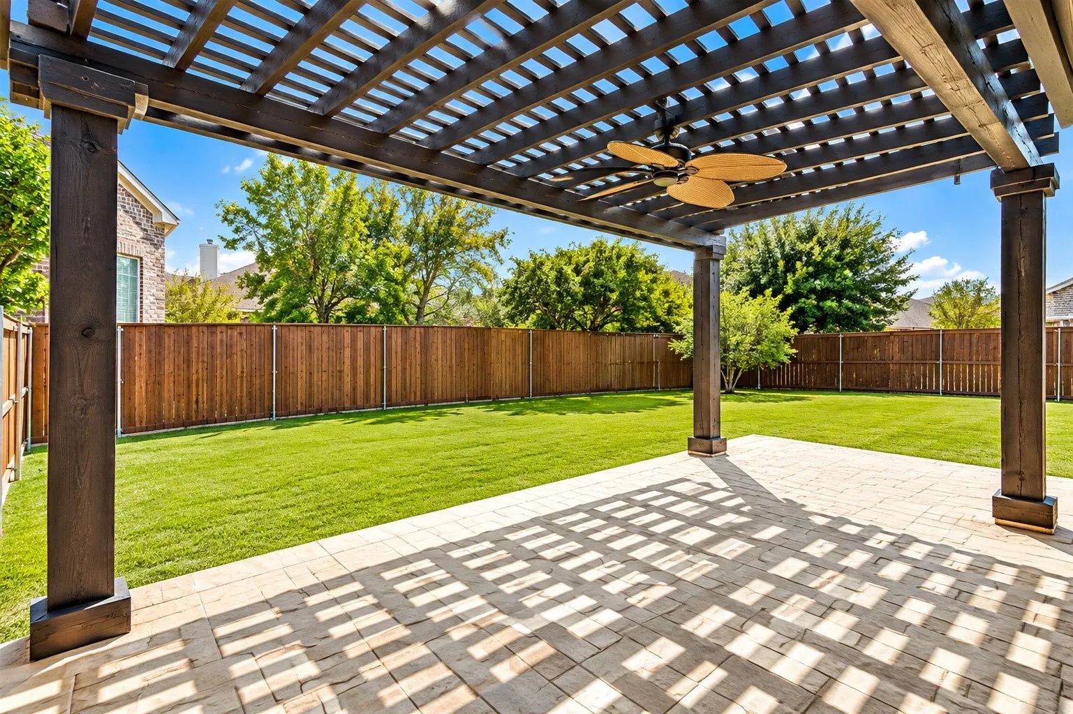 Expansive backyard featuring a wood pergola, integrated ceiling fan, paver patio, and manicured lawn