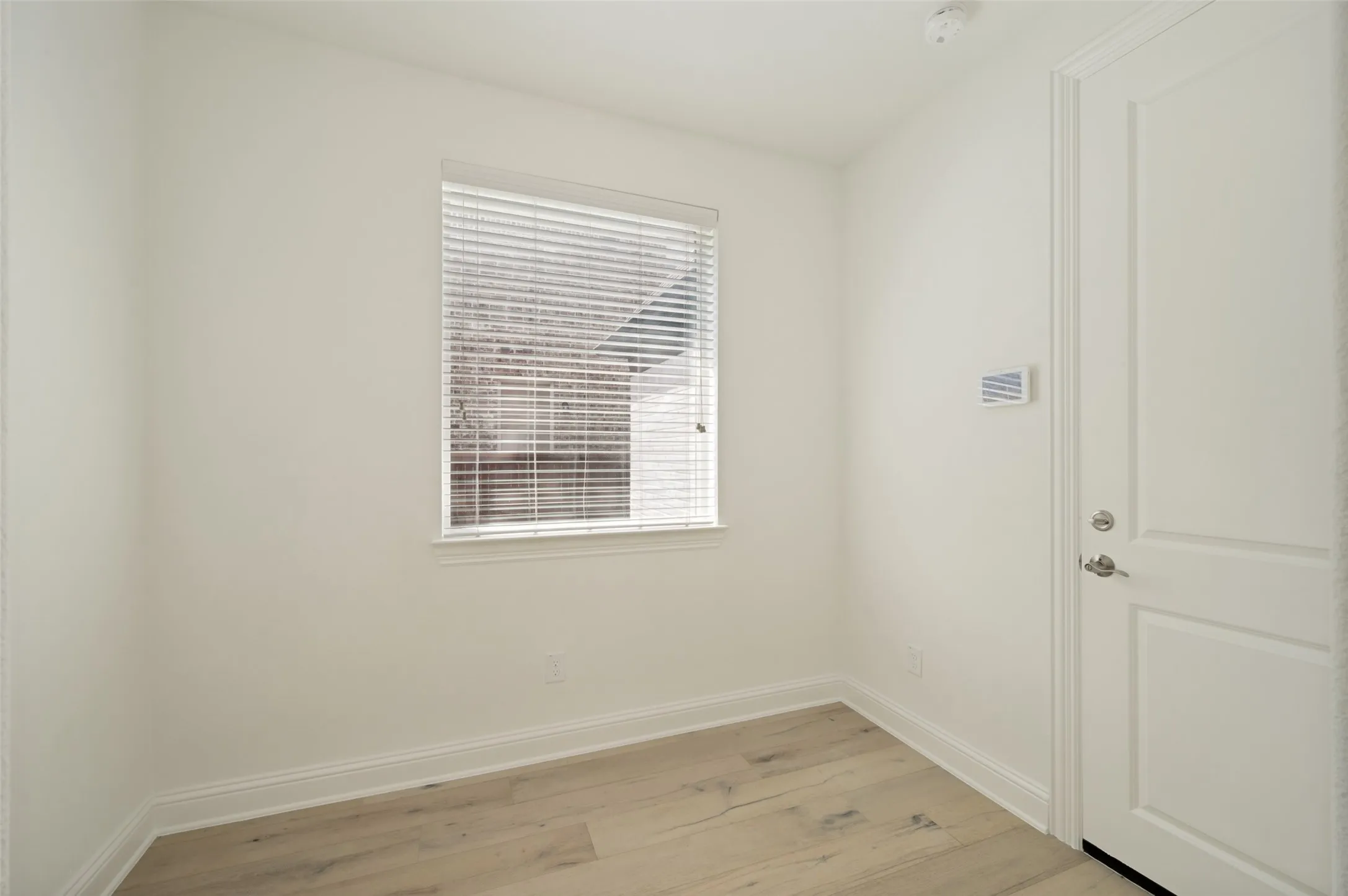 Light wood-finish flooring, white walls, and a window with horizontal blinds