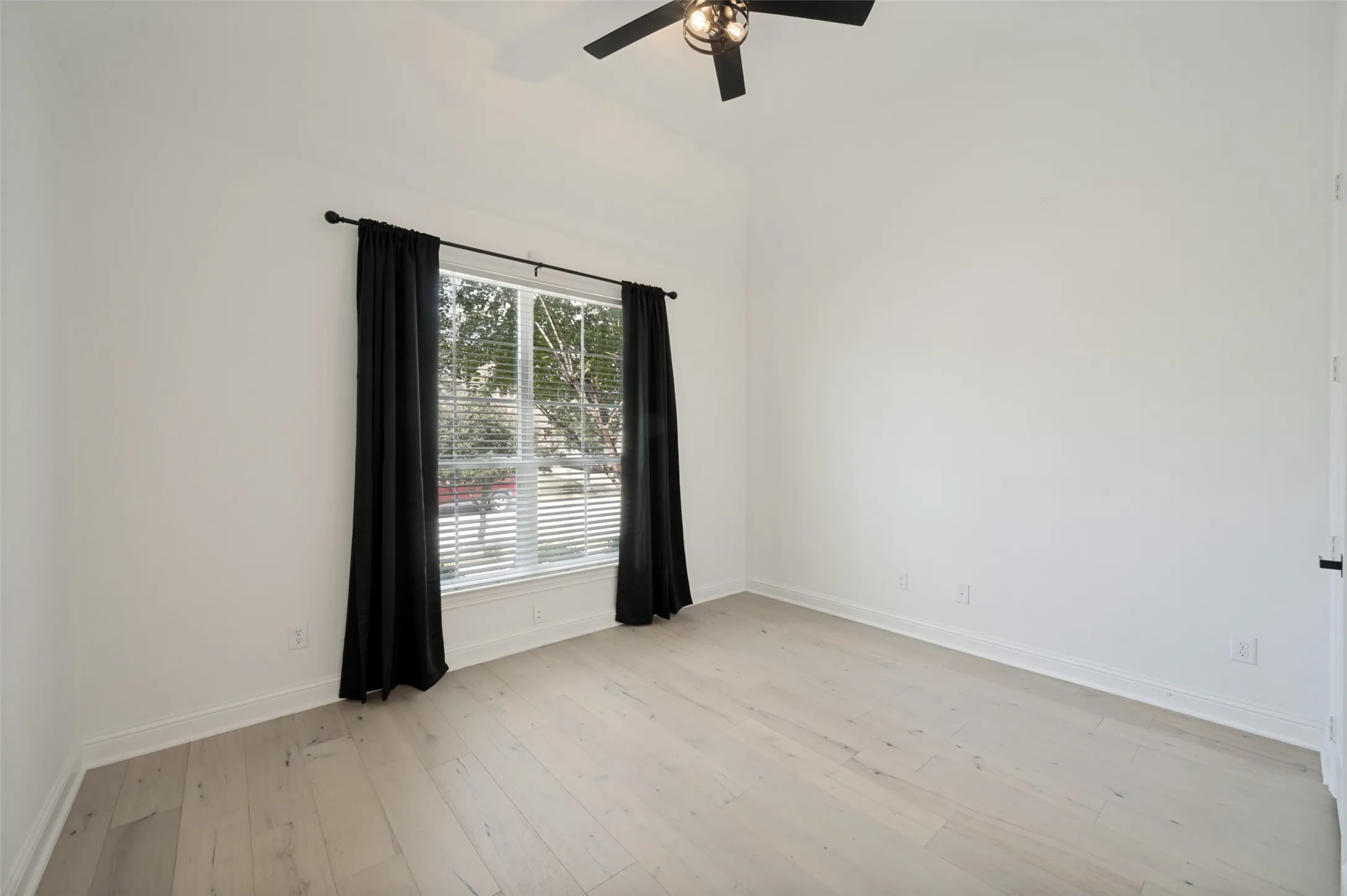 Wood-finish flooring with white baseboards, a ceiling fan with integrated lighting, and a window with blinds and dark drapery