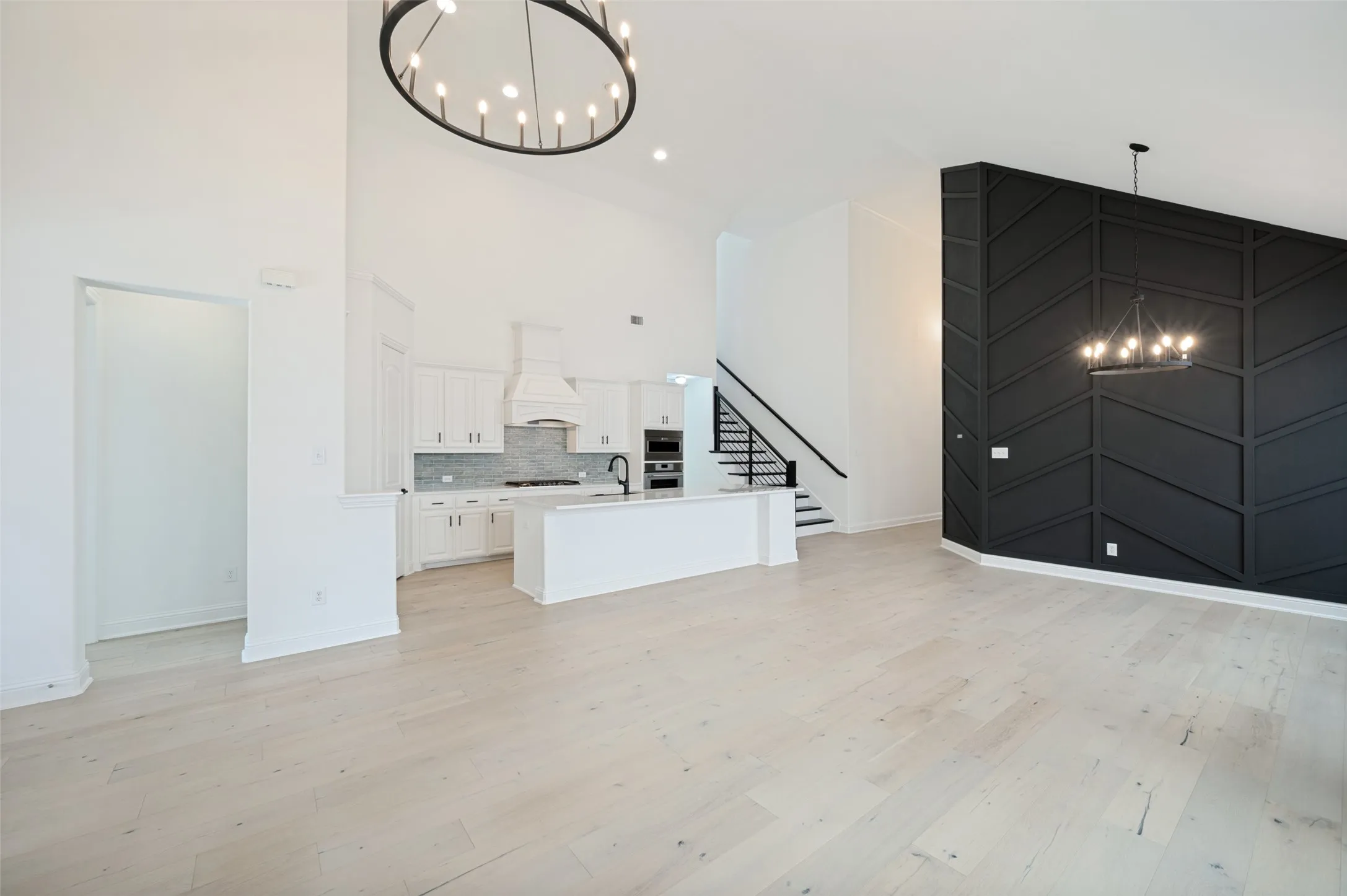 Vaulted ceilings with a contemporary chandelier, light wood-finish flooring, and a kitchen featuring white cabinetry, a large island, and a tile backsplash
