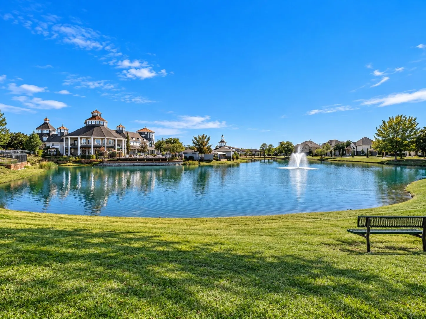 Expansive lake with a central fountain, manicured green space, and a community building with covered balconies