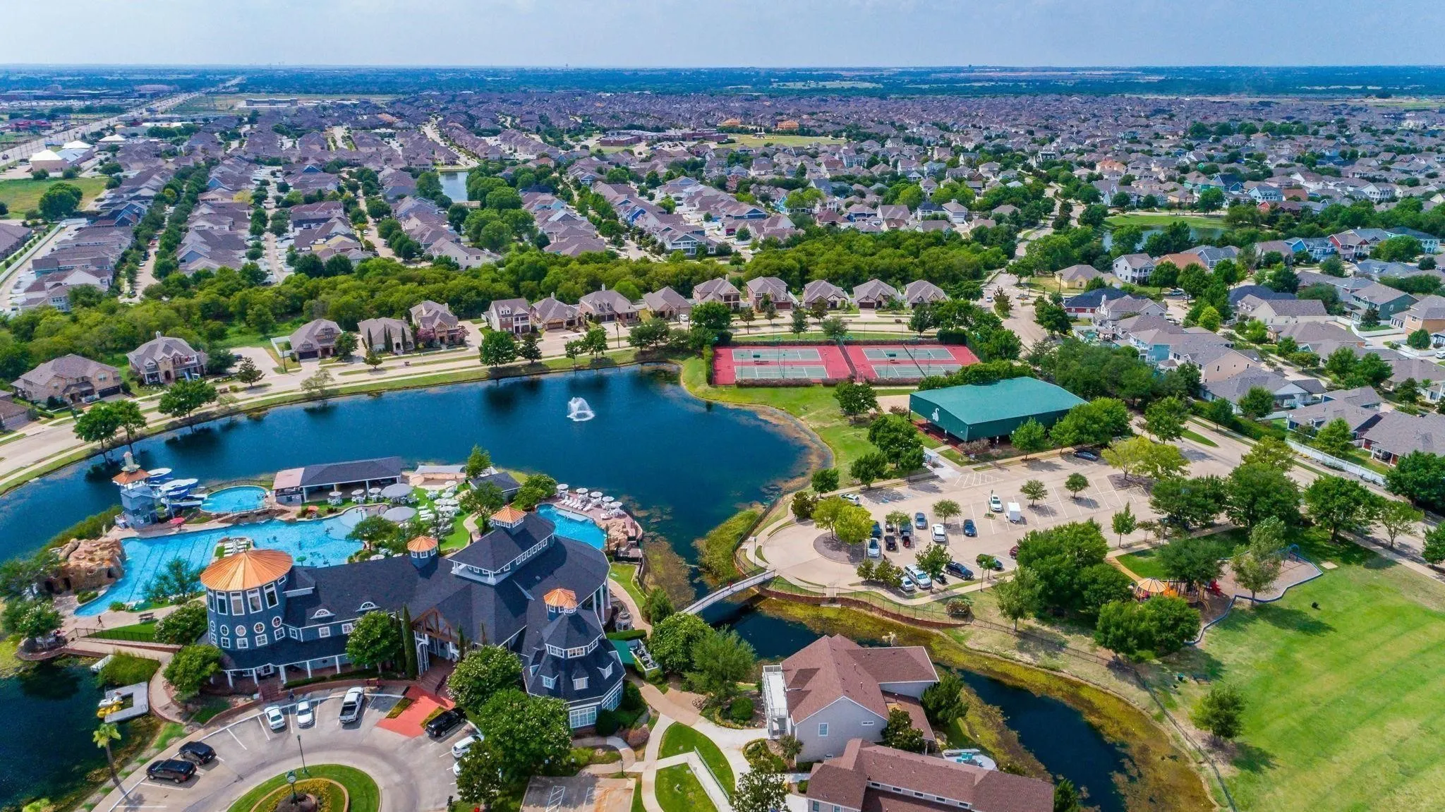 Expansive community featuring a large lake, clubhouse, swimming pool area, tennis courts, and surrounding residential properties