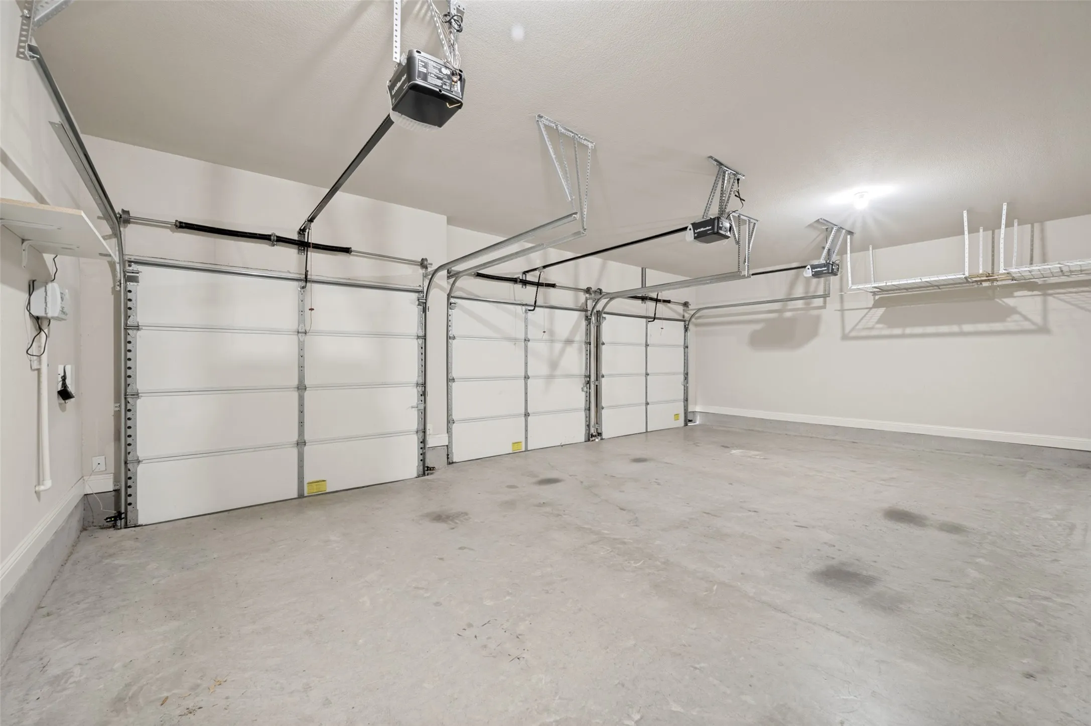 Three-car garage with concrete flooring, automatic garage door openers, and overhead storage shelving