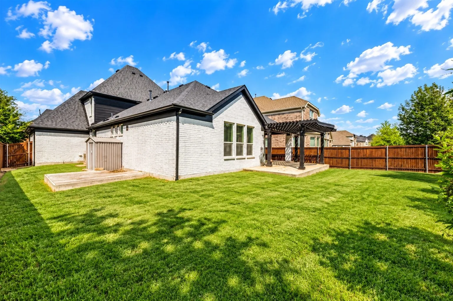 Expansive backyard featuring a manicured lawn, a wooden deck, and a patio with a dark-stained pergola