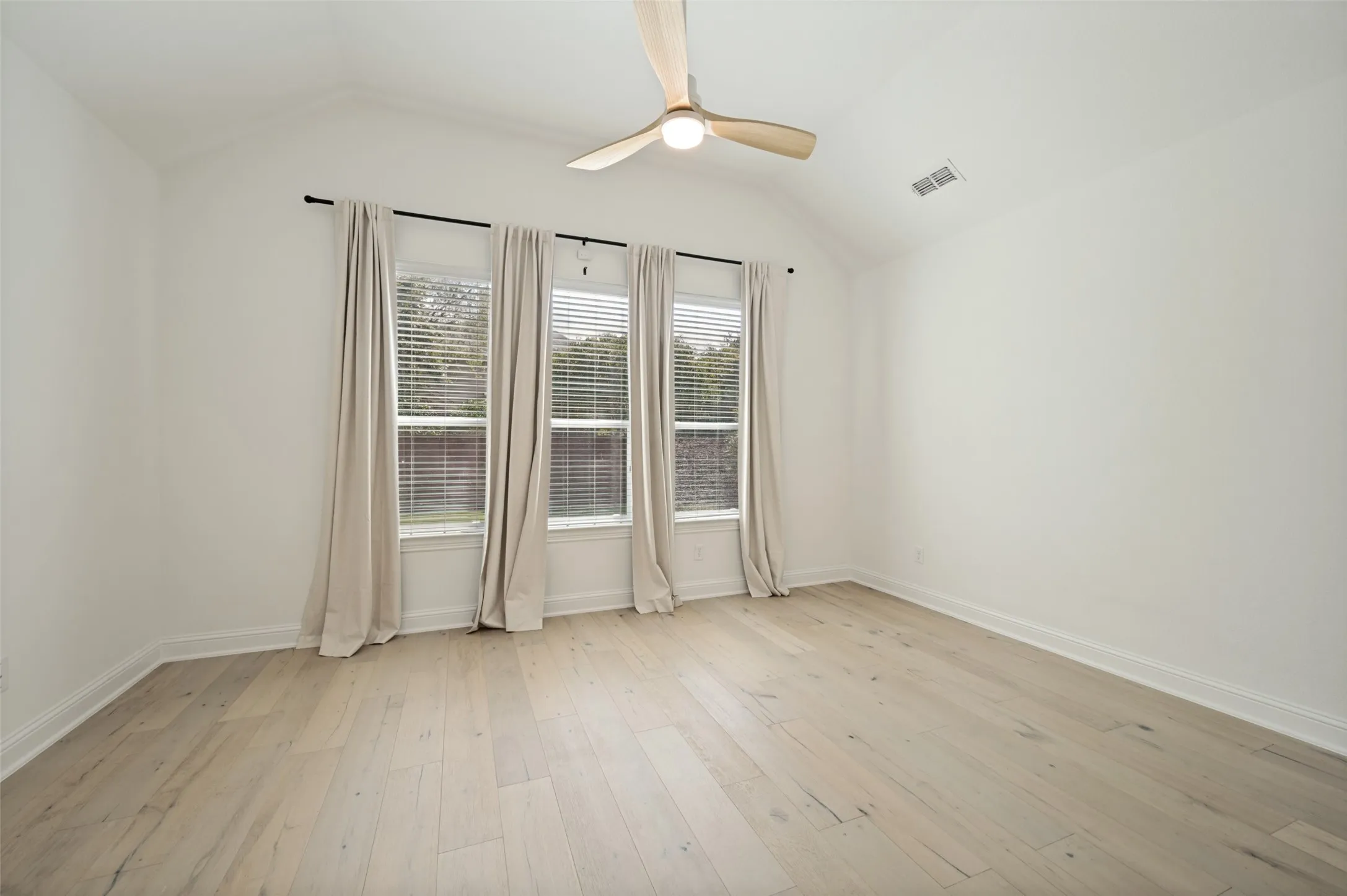 Vaulted ceiling with an integrated ceiling fan, light wood-finish flooring, and multiple windows with blinds