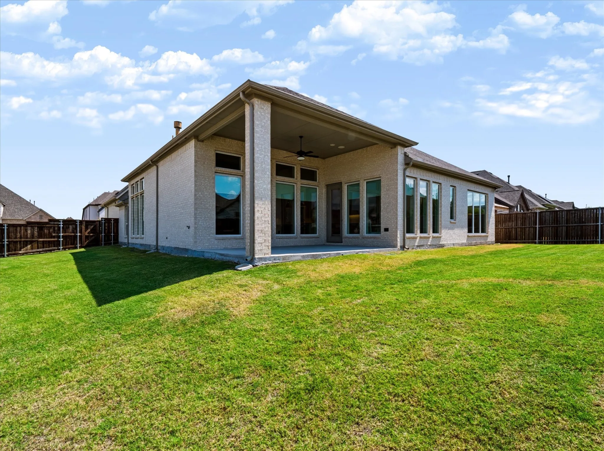 Expansive backyard with a manicured lawn, full privacy fencing, and a covered patio featuring a ceiling fan