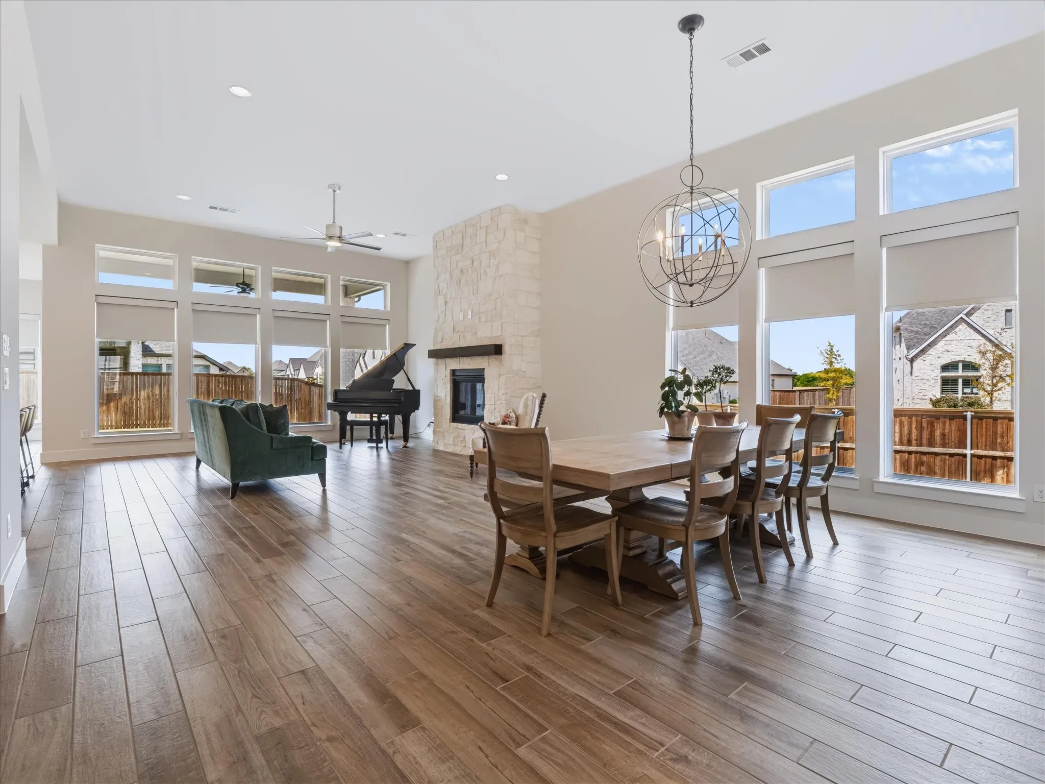 Expansive open-concept living space with high ceilings, wood-finish flooring, a stone-clad fireplace with wood mantle, and extensive window arrays