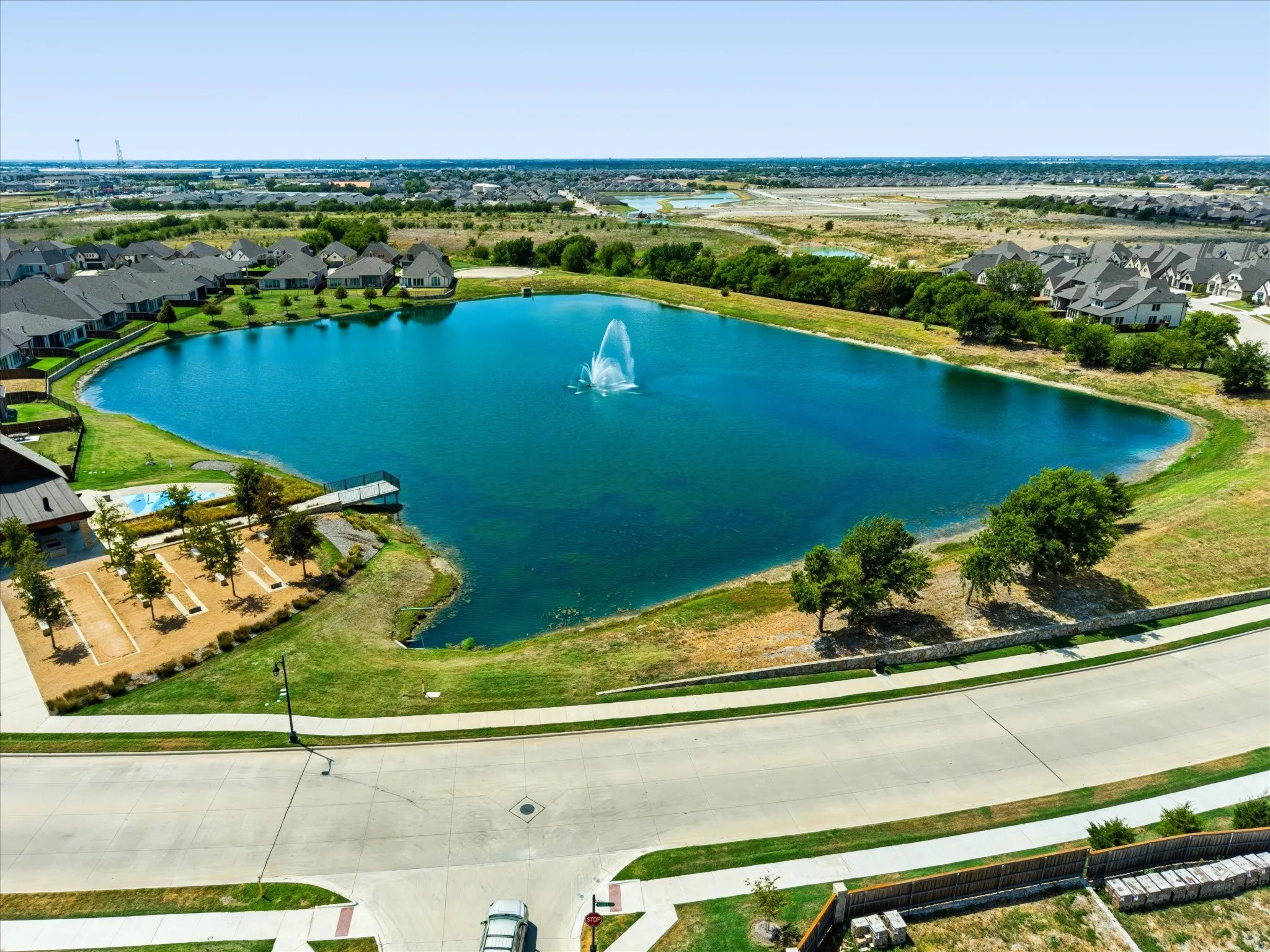 Expansive lake with a central fountain, surrounding green spaces, and a nearby community pool
