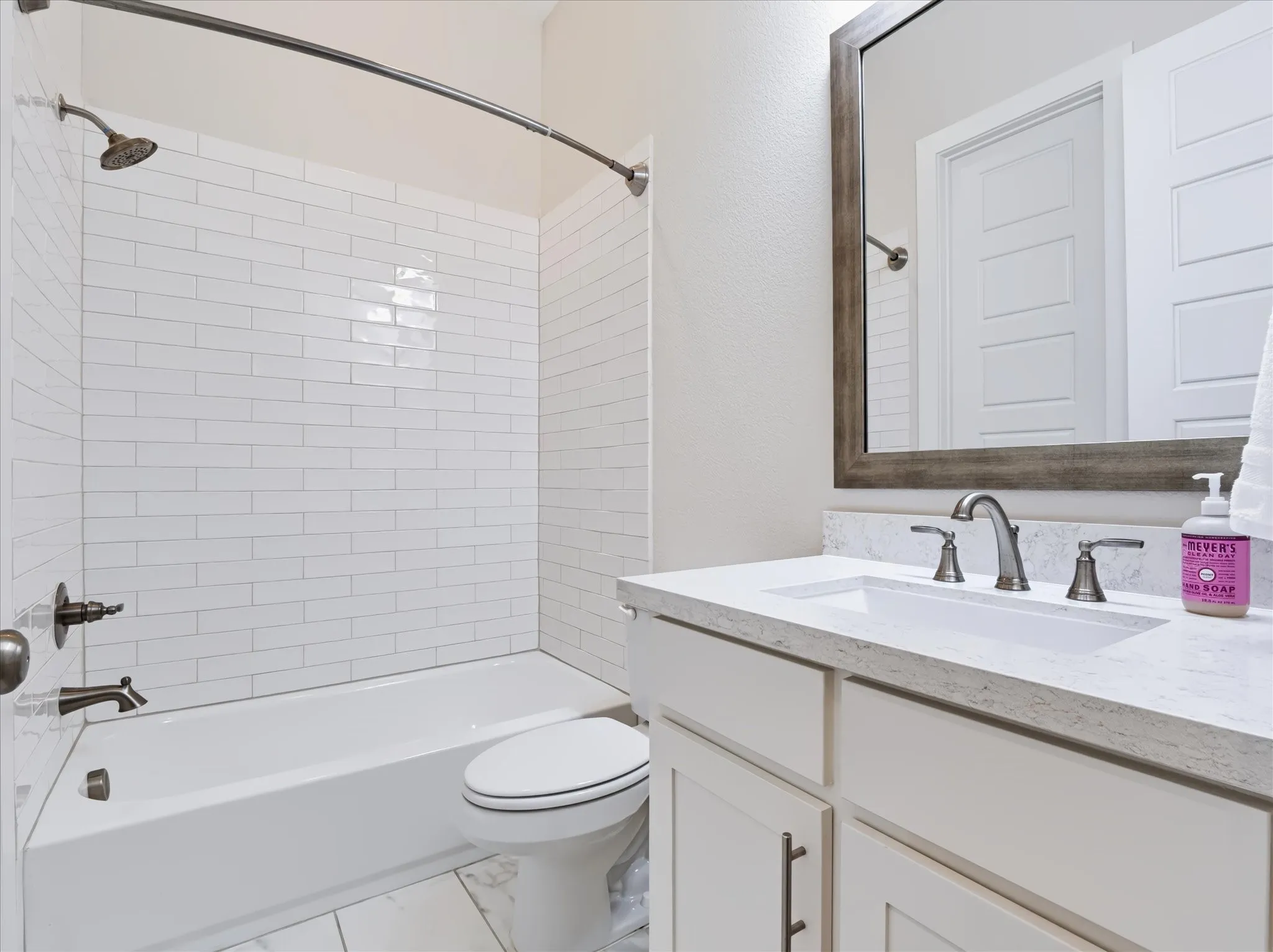 White subway tile shower surround, white bathtub, white vanity with integrated sink, silver-toned fixtures, and a framed mirror
