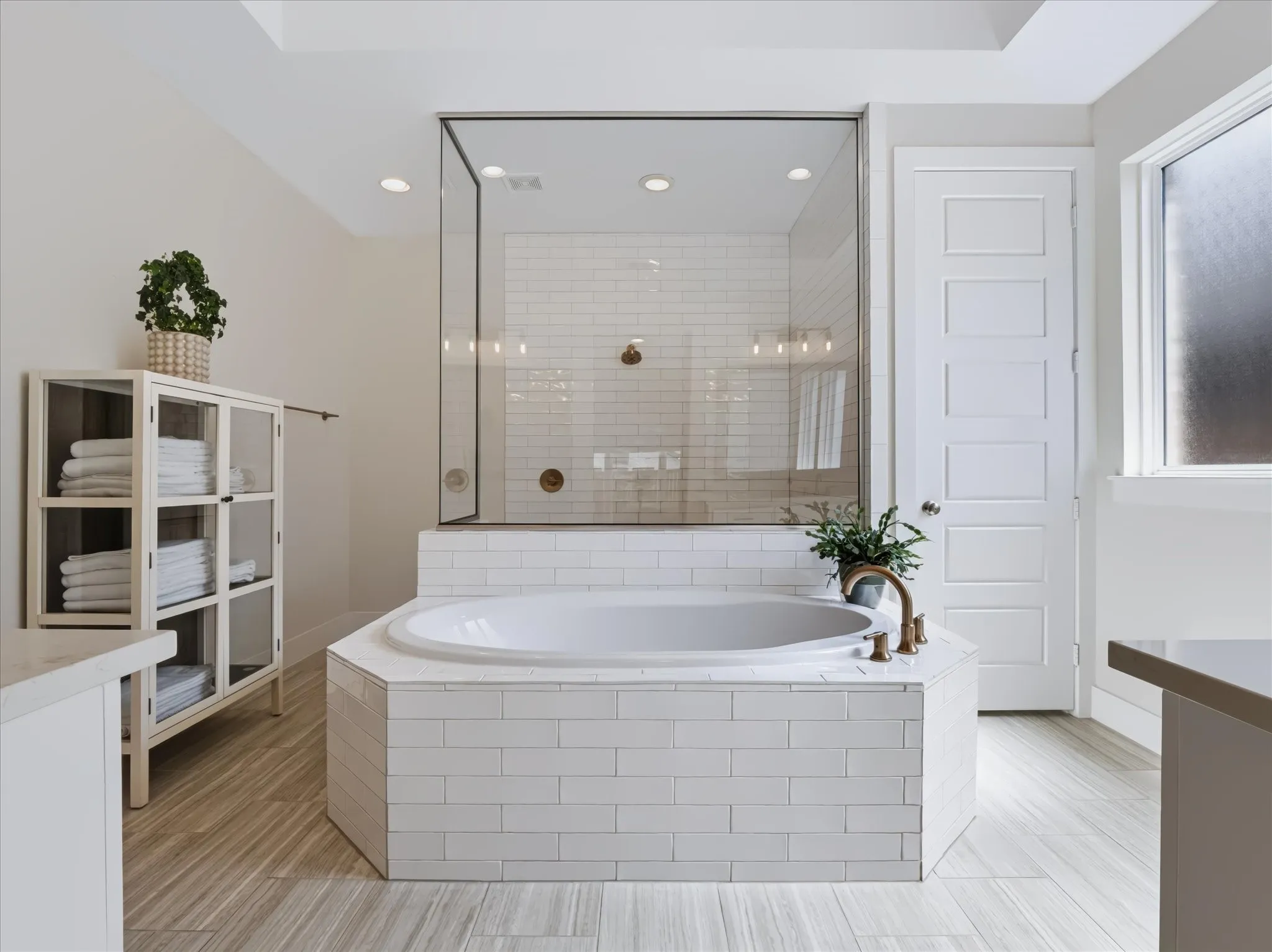 White subway tile surround for the soaking tub, a frameless glass shower enclosure, wood-finish flooring, a contemporary paneled door, and a frosted window
