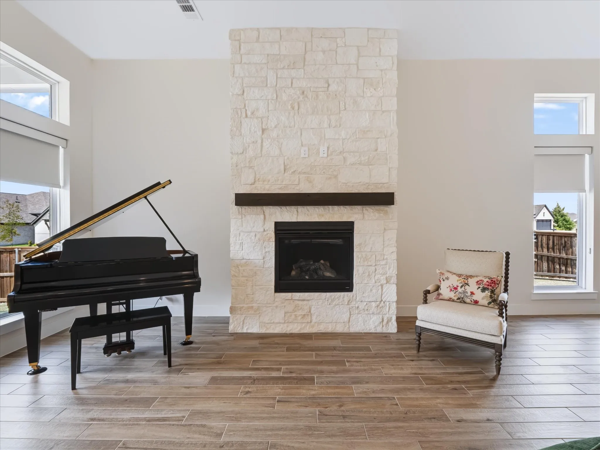 Tiled flooring throughout, stone-clad fireplace with dark wood mantel, and tall windows with transom architectural details