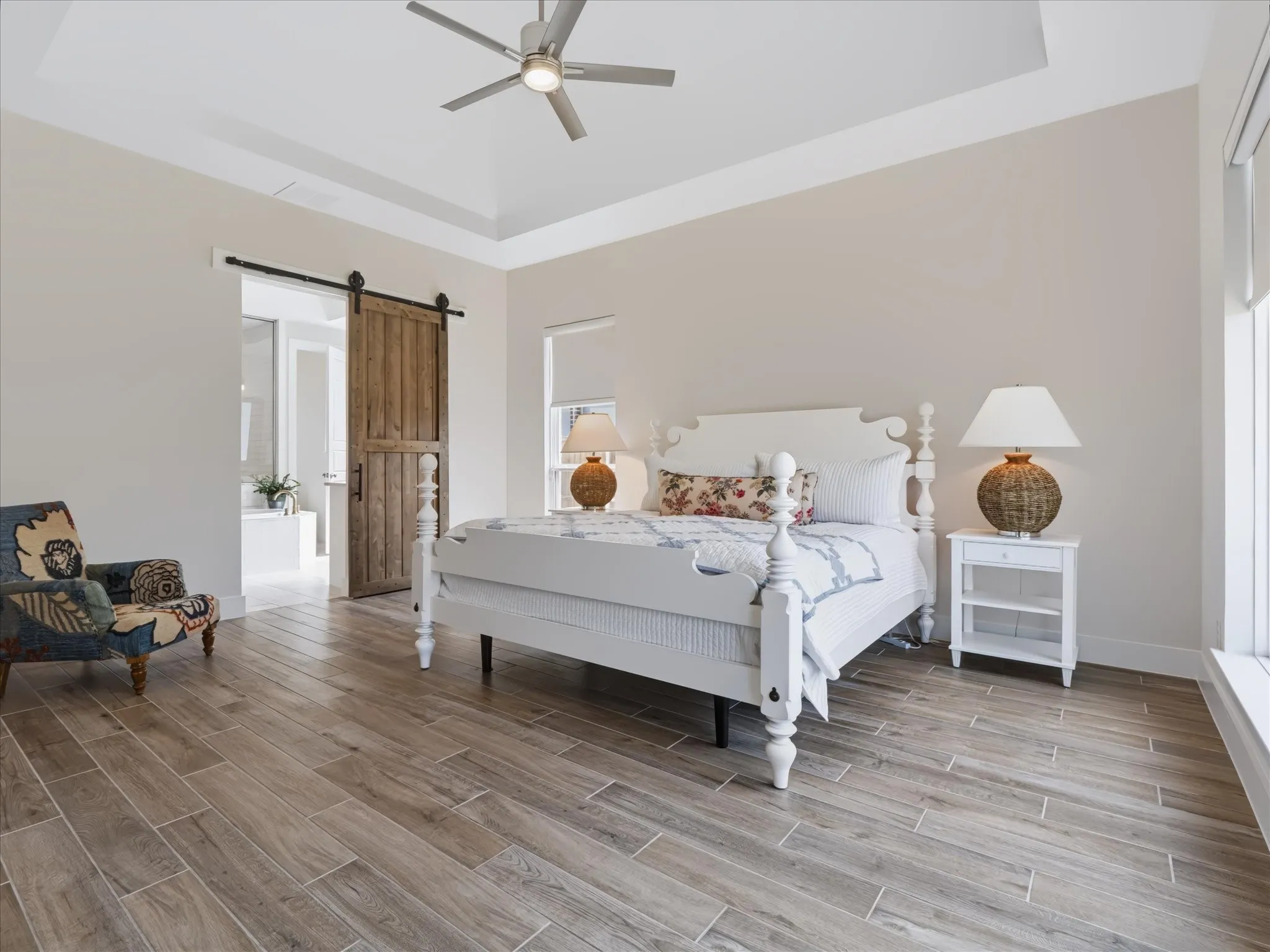 Tray ceiling with a ceiling fan, wood-finish flooring, and a sliding barn door