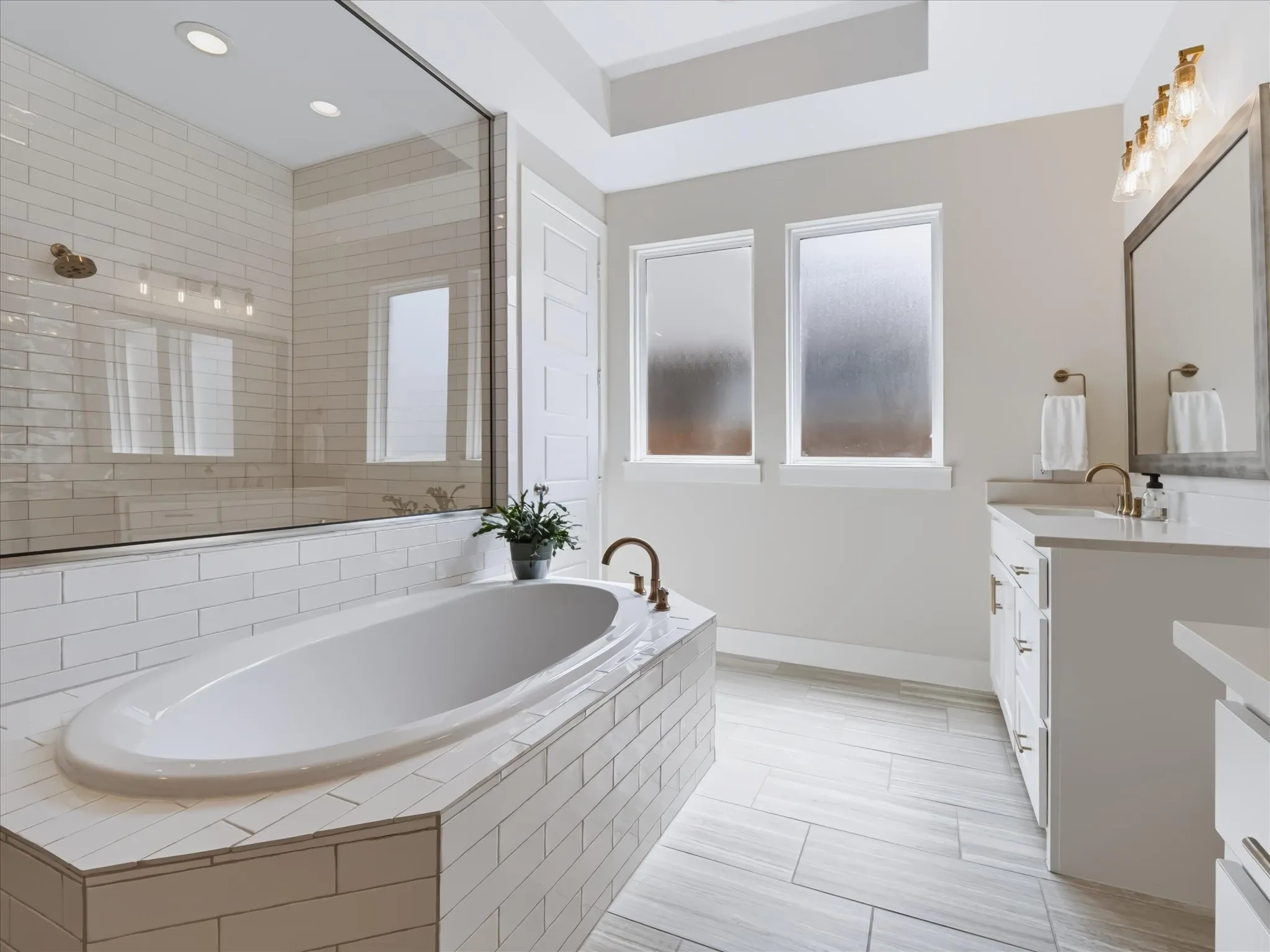 Freestanding soaking tub with subway tile surround, clear glass shower enclosure, dual vanity with quartz countertops, framed mirror, and tile flooring