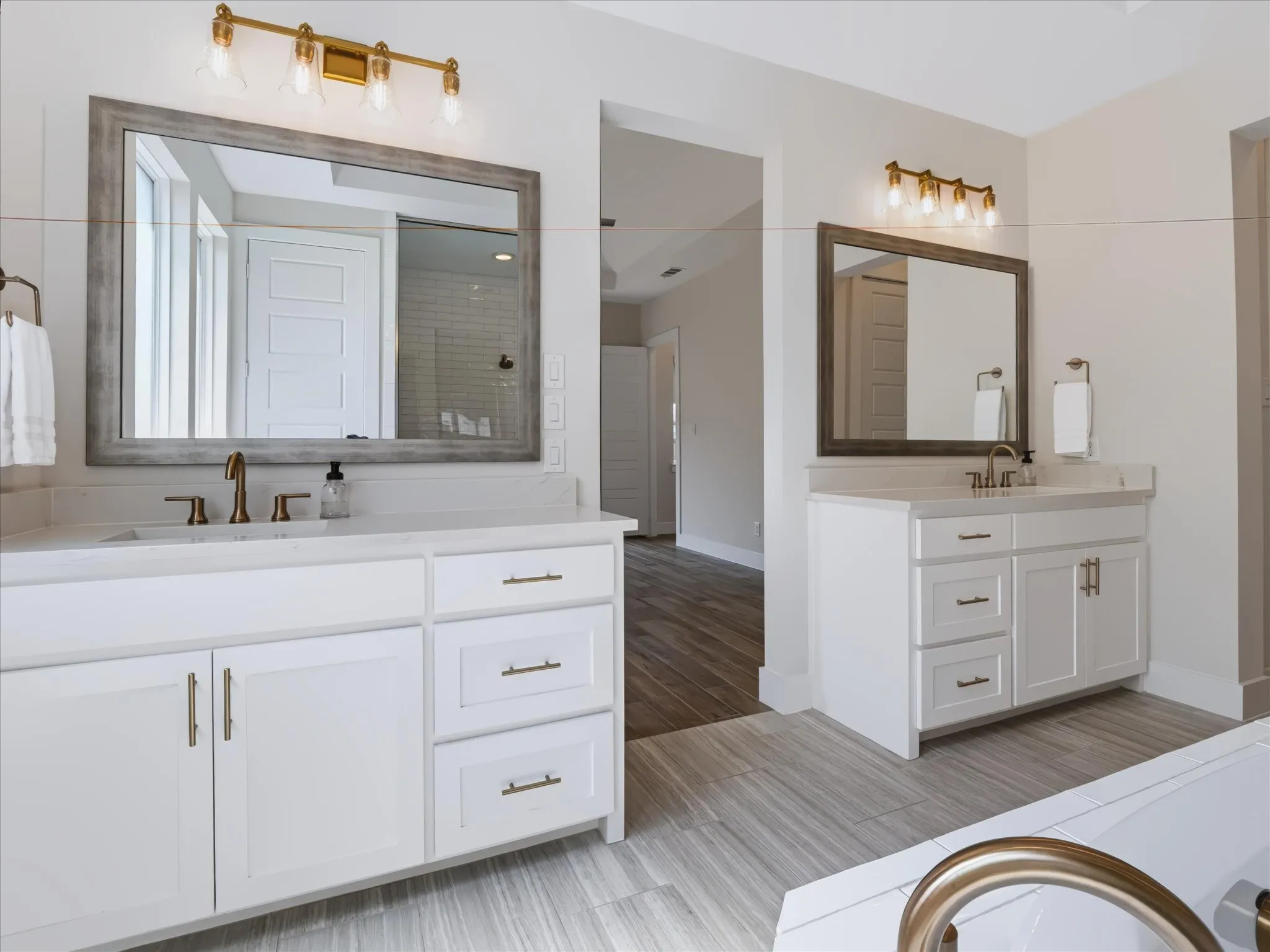 Dual vanity with white cabinetry, quartz-finish countertops, brass-finish fixtures, and framed mirrors