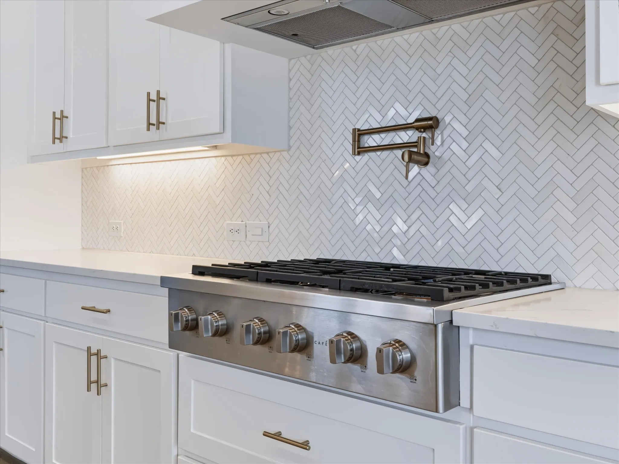 White shaker cabinetry, herringbone tile backsplash, stainless steel range with griddle, pot filler, and light-toned countertops
