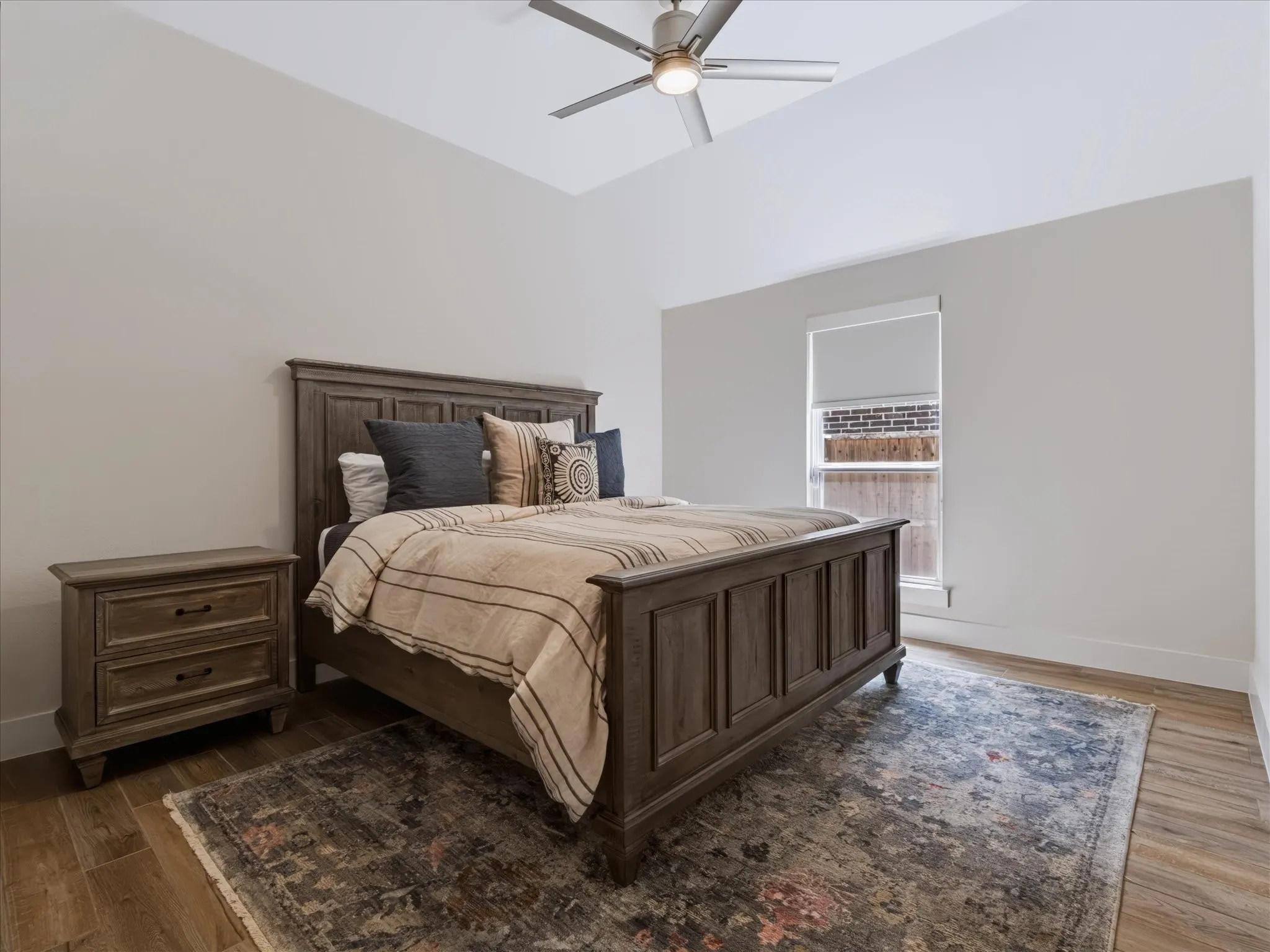 Vaulted ceiling with a ceiling fan, wood-finish flooring, and a large window
