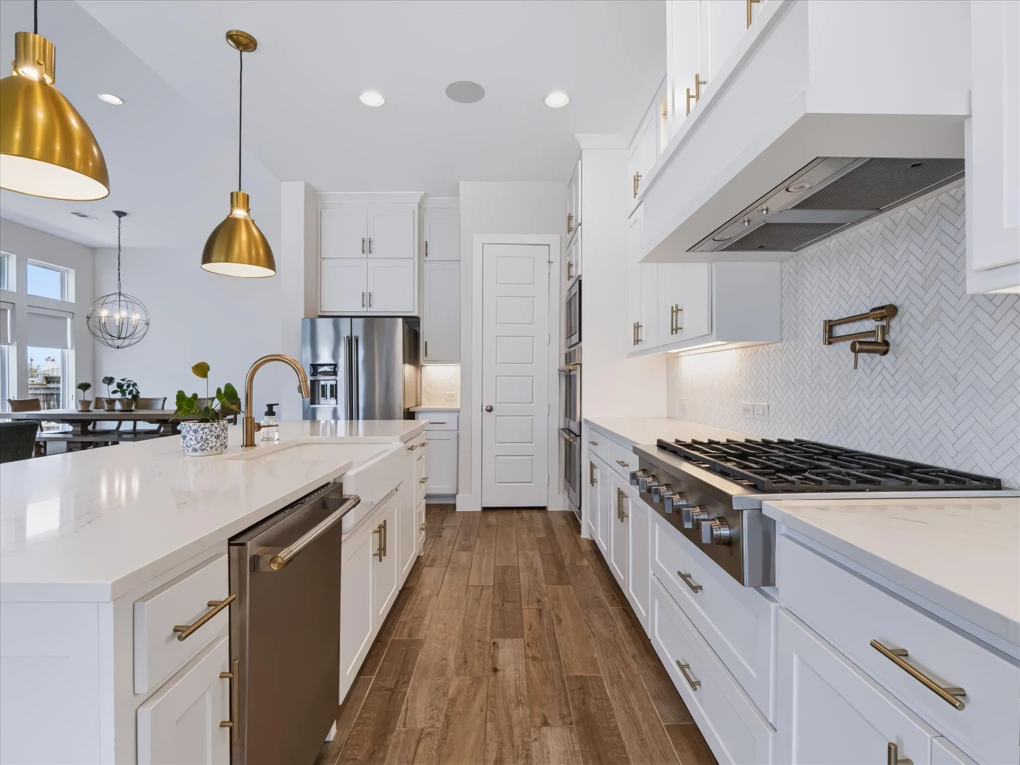 Gourmet kitchen with wood-finish flooring, white shaker cabinetry, stainless steel appliances, a large center island, and white quartz countertops