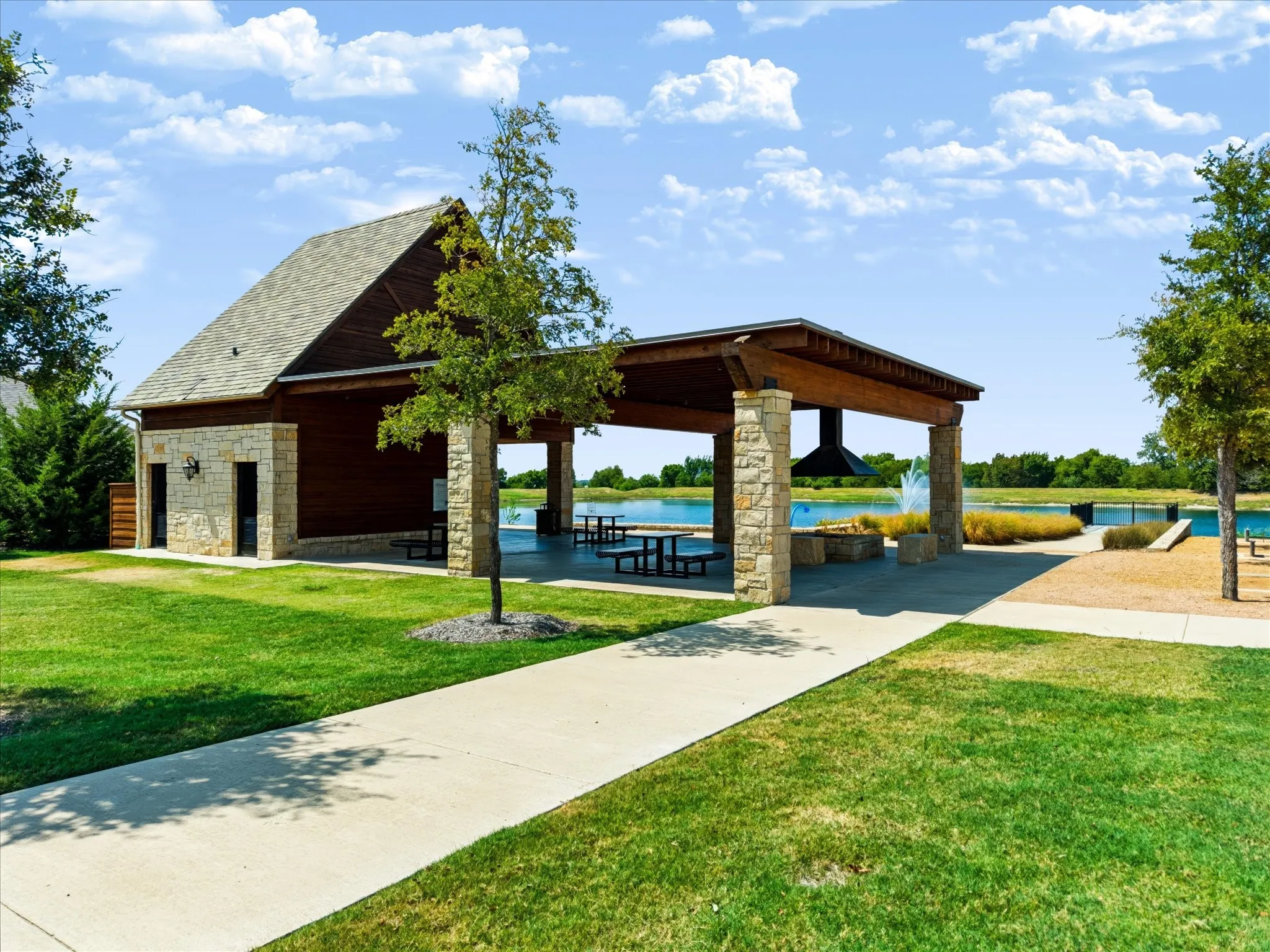 Stone and wood-finish pavilion with a large built-in fireplace, concrete walkways, and a manicured lawn