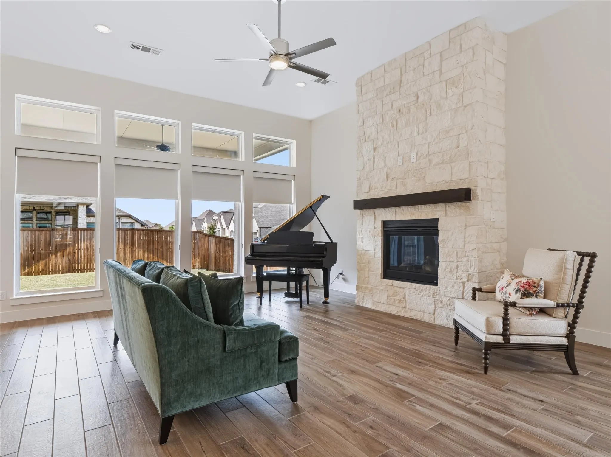 Floor-to-ceiling windows with roller shades, stone-clad fireplace with wood mantle, wood-finish tile flooring, recessed lighting, and a ceiling fan