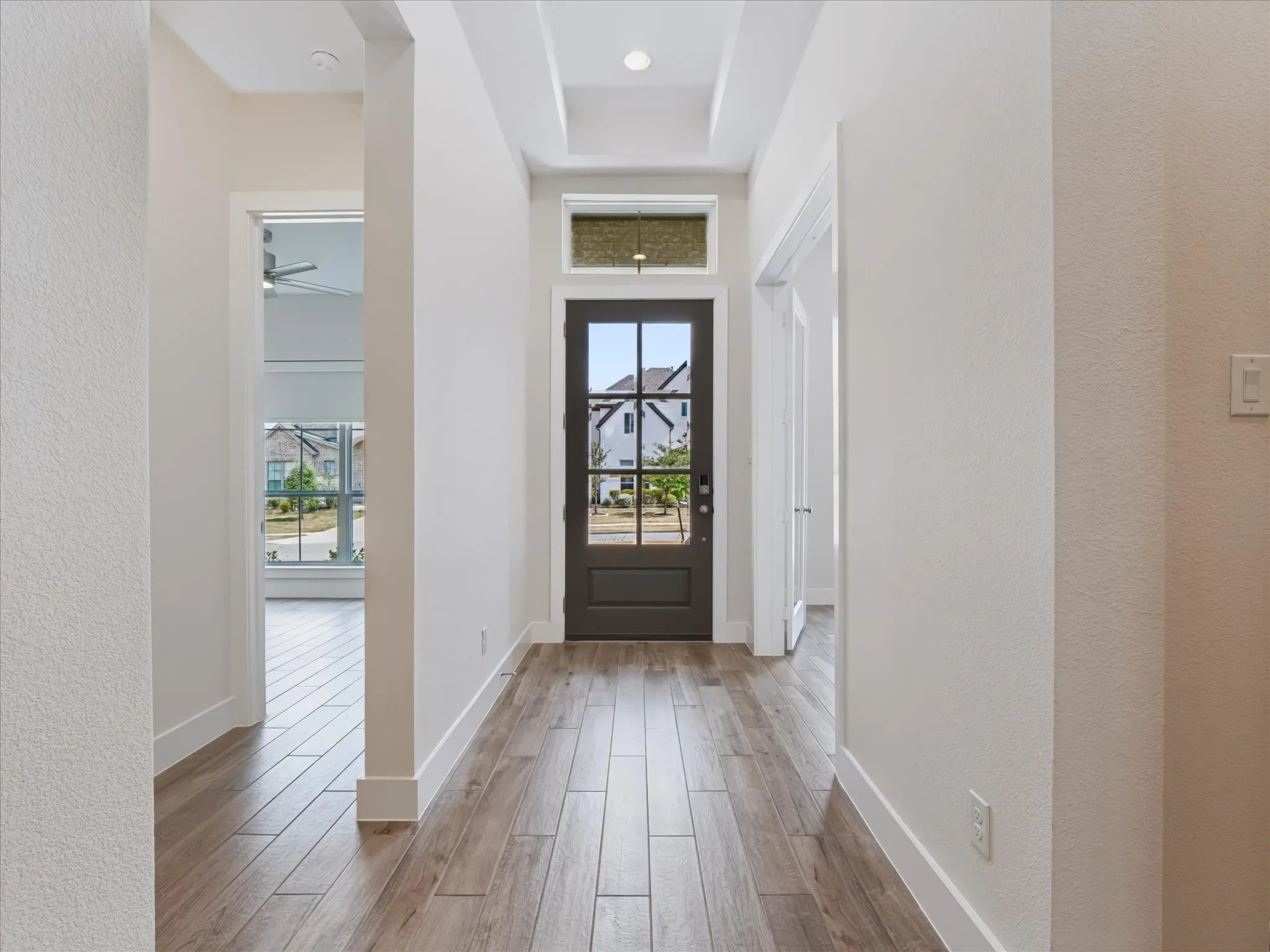 Entryway featuring wood-finish flooring, a dark-paneled front door with clear glass, a transom window, and recessed lighting