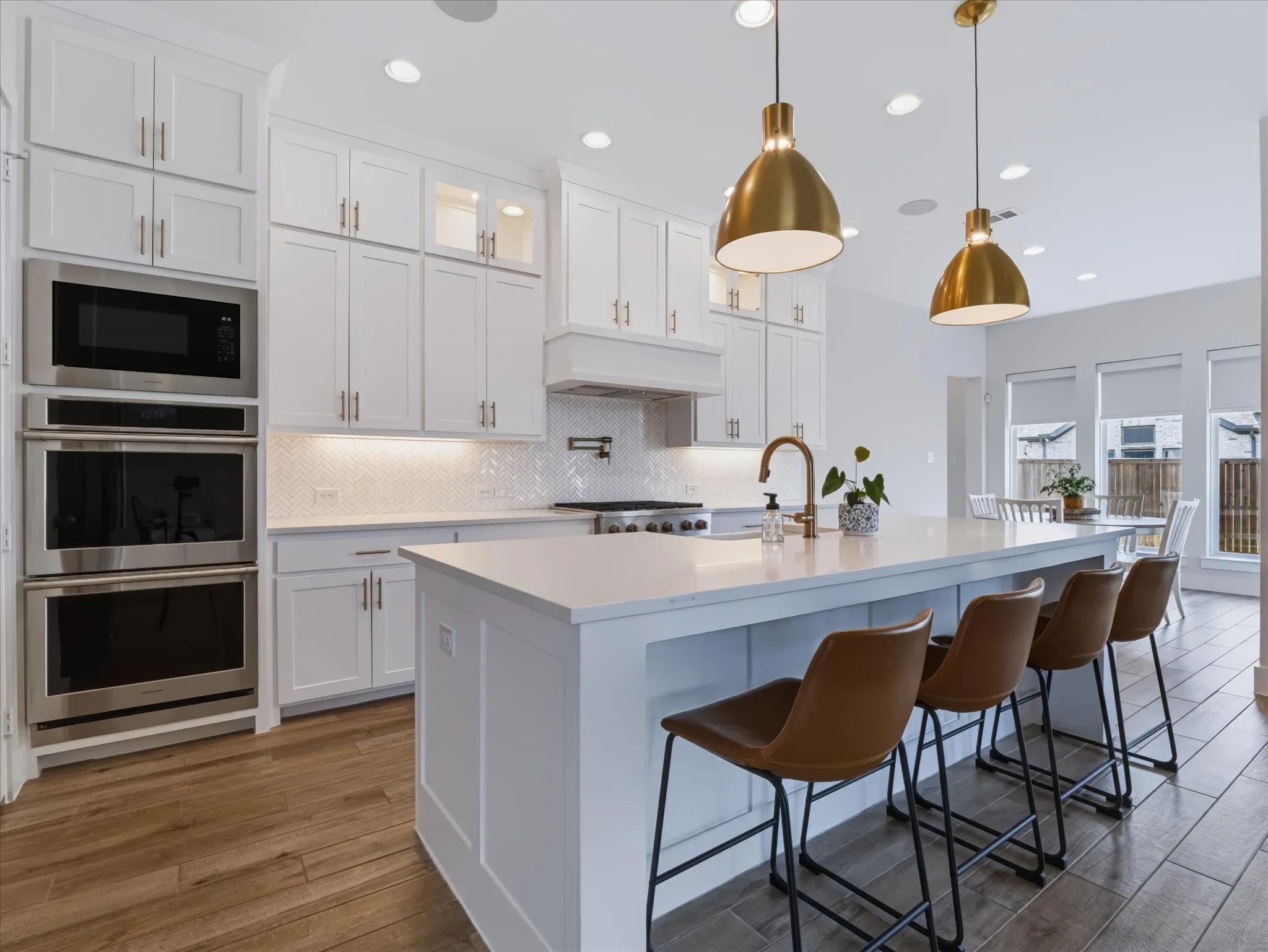 Gourmet kitchen featuring white cabinetry, stainless steel double ovens, a built-in microwave, a central island with counter seating, and wood-finish flooring