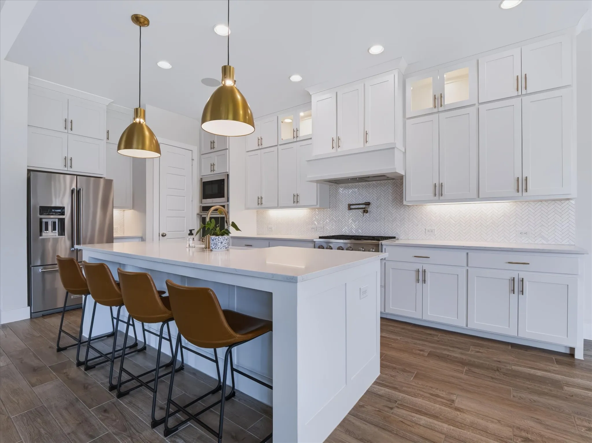 Center island with seating, stainless steel appliances, white shaker cabinetry, herringbone tile backsplash, and wood-finish flooring