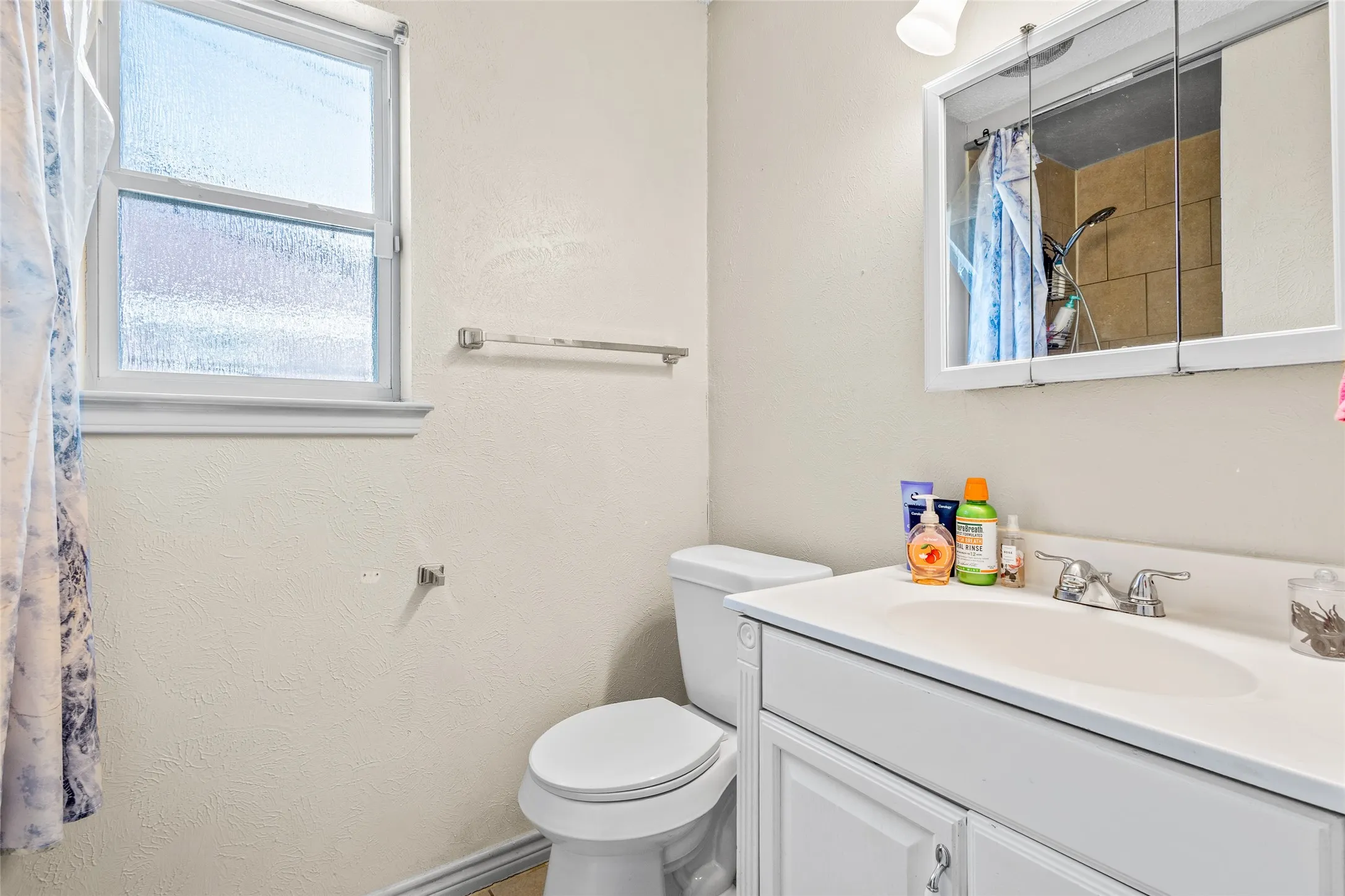White vanity with integrated sink, chrome faucet, medicine cabinet, and frosted window