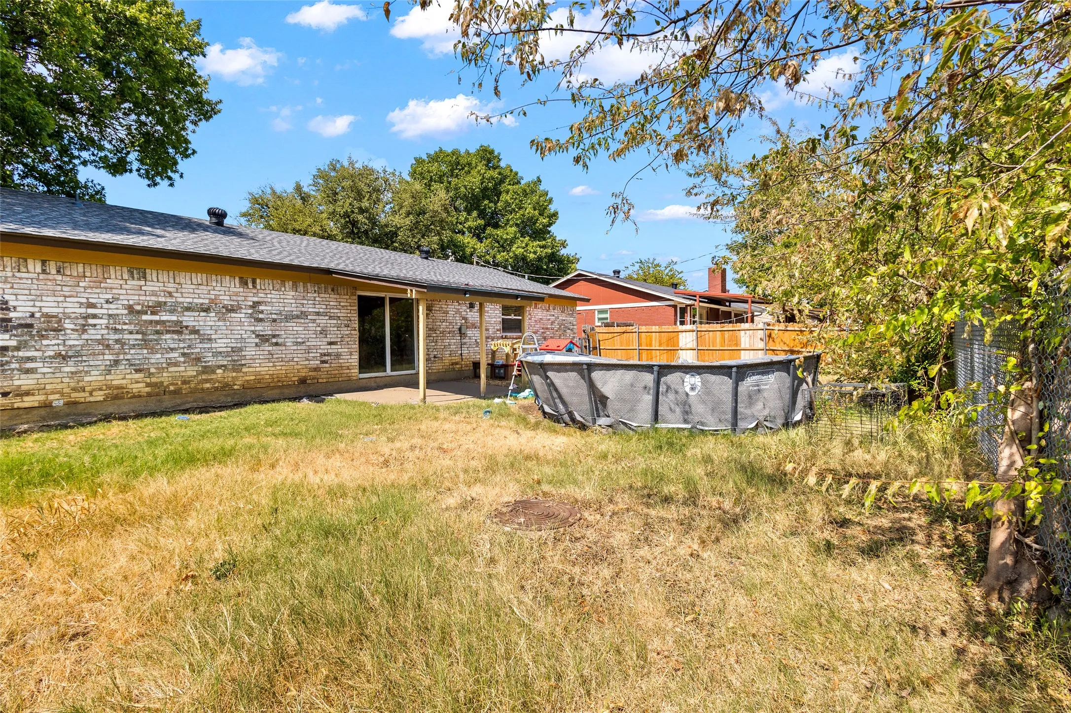 Brick exterior with a covered patio, sliding glass door, and an above-ground pool