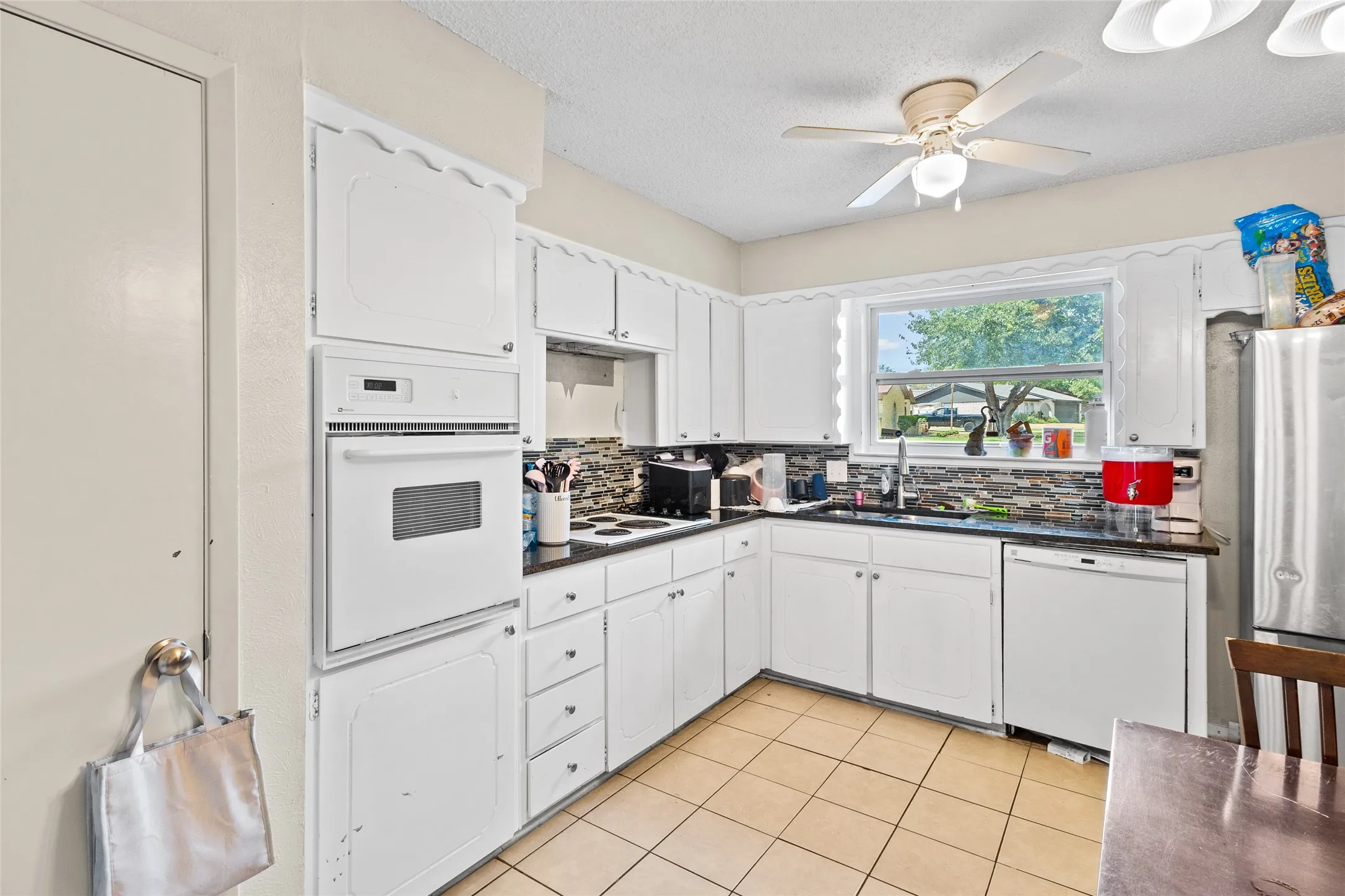 Kitchen featuring white cabinetry, dark countertops, built-in oven, tile flooring, and a ceiling fan