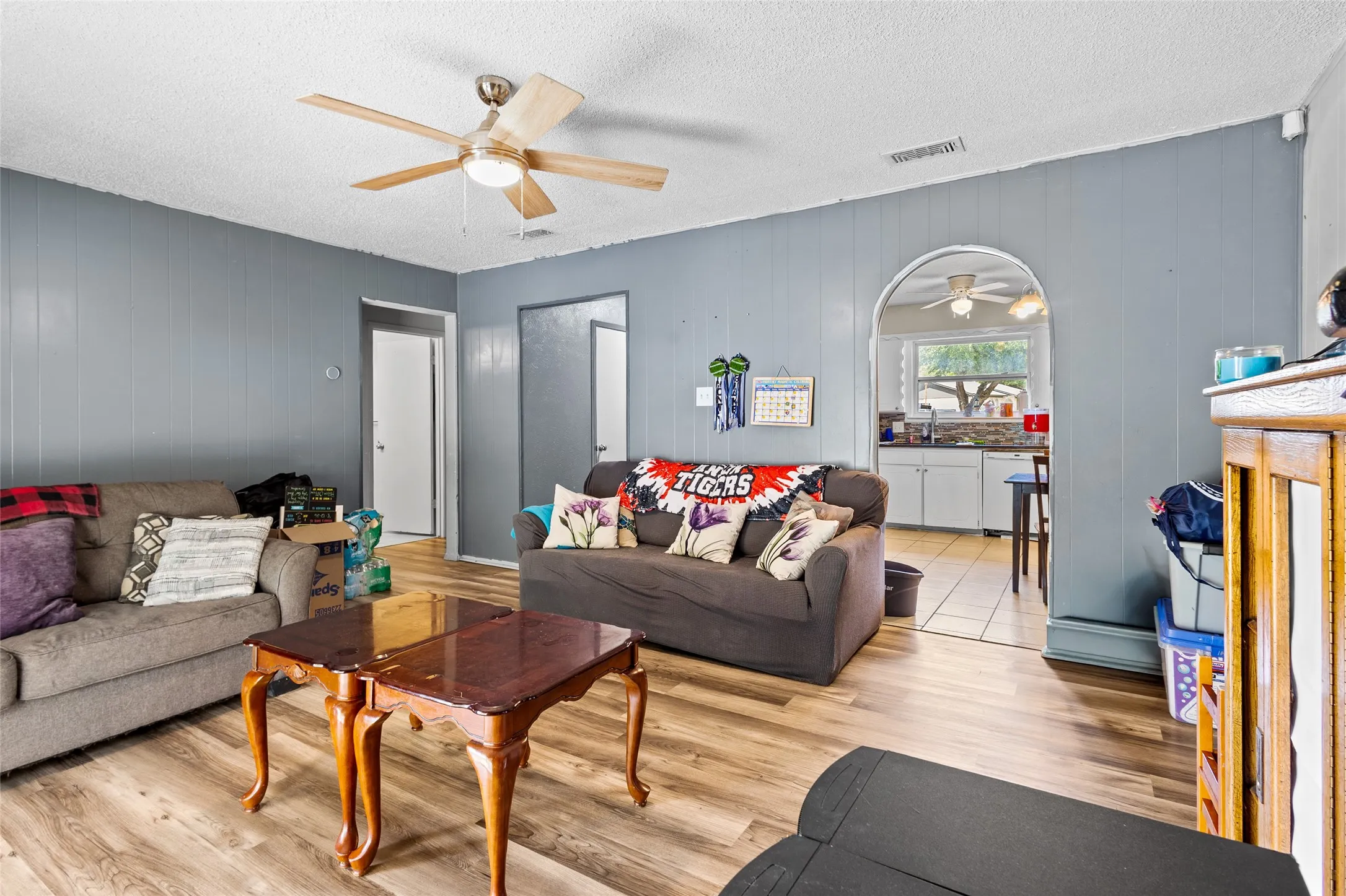 Wood-finish flooring throughout, ceiling fan with light fixture, and an arched doorway