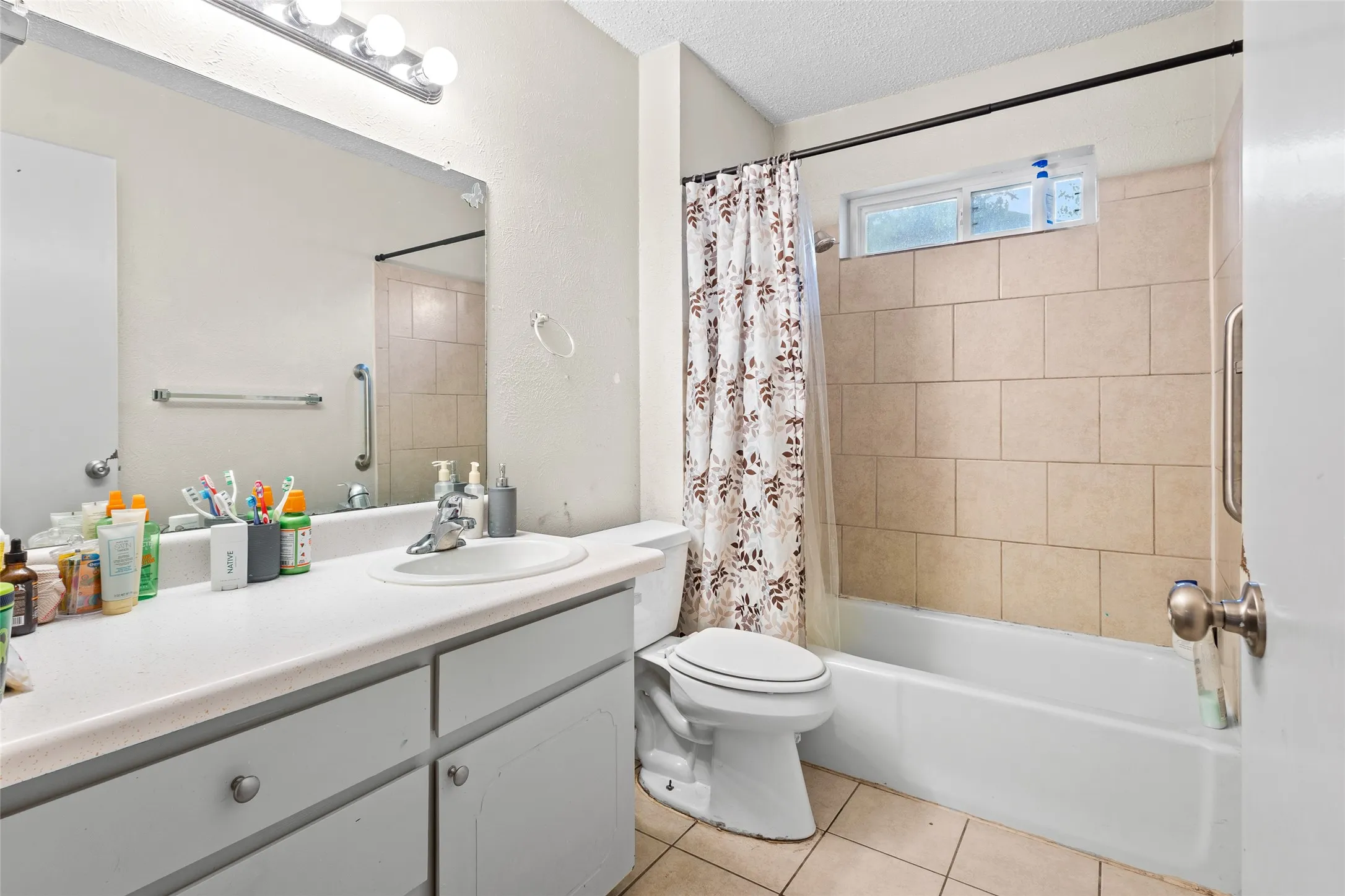 Bathroom featuring a vanity with an integrated sink, a large wall mirror, a tiled shower/tub combination, and a window for natural light