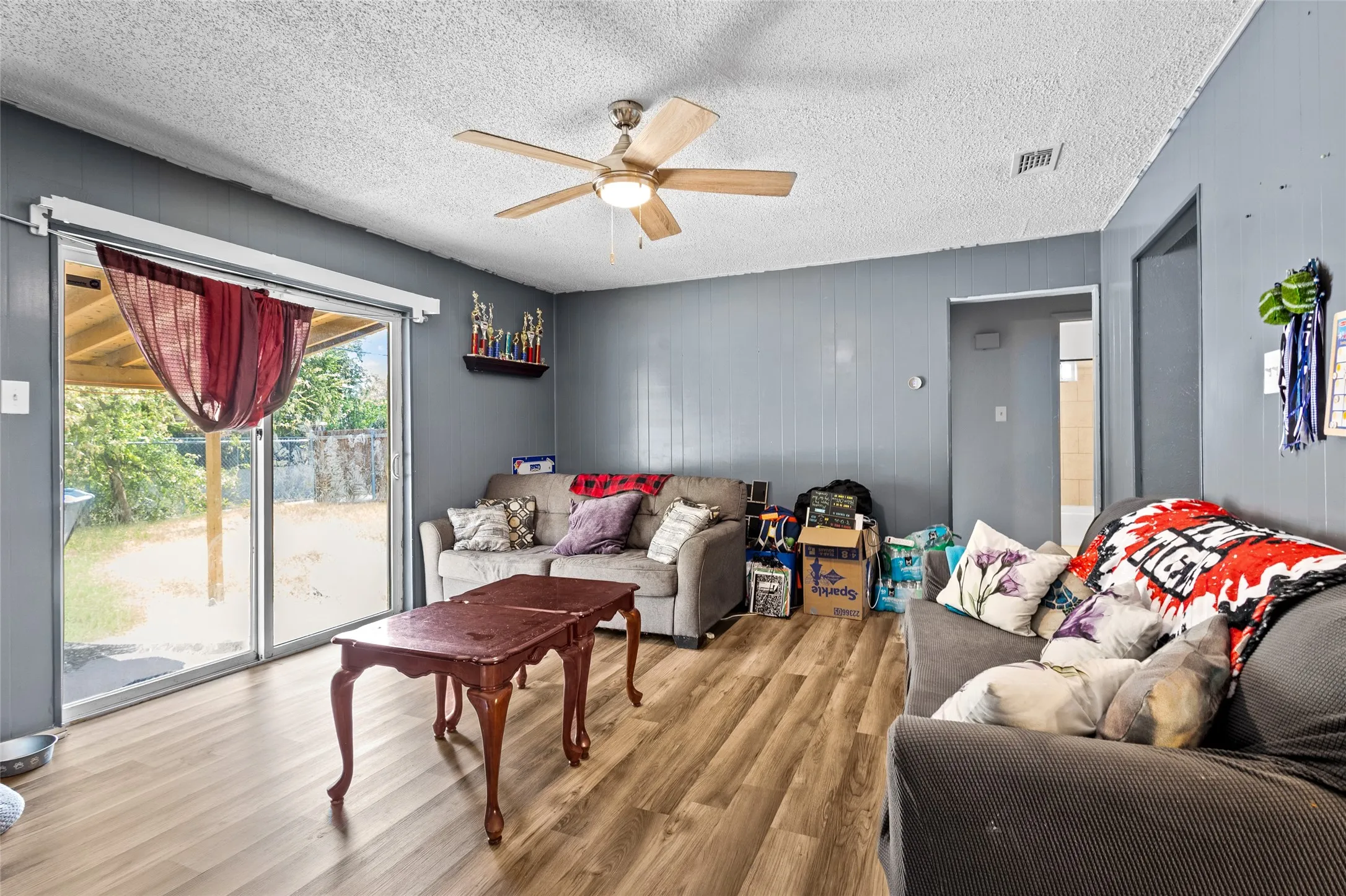 Wood-finish flooring, sliding glass door with exterior access, ceiling fan with integrated lighting, and paneled walls