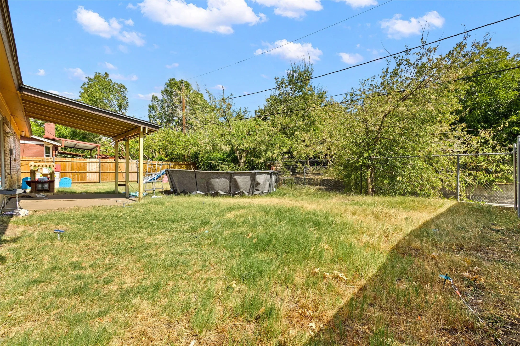 Expansive backyard featuring a covered patio, chain-link fencing, and mature trees