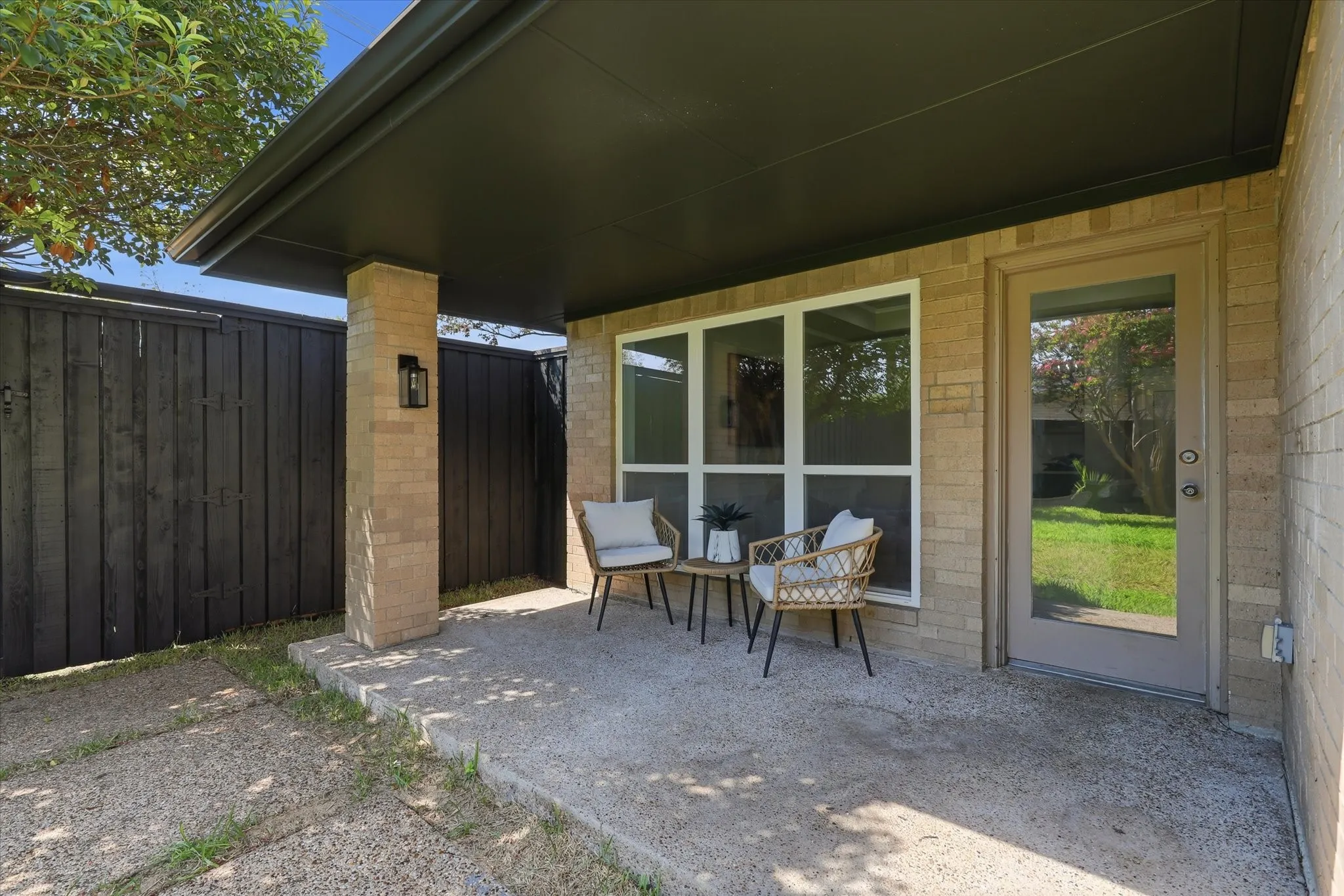 Covered patio with a concrete surface, brick column, and black privacy fence