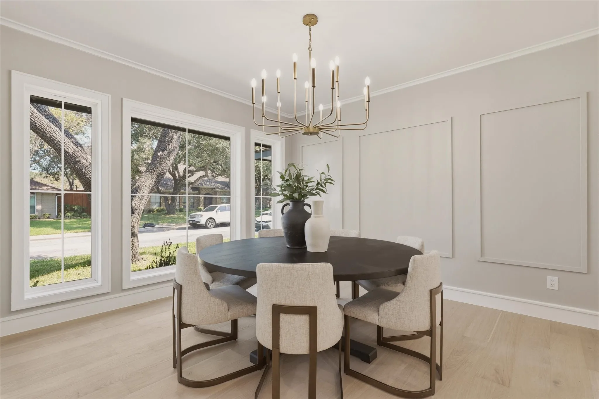 Spacious room featuring multiple large windows, a distinctive chandelier, and light wood-finish flooring