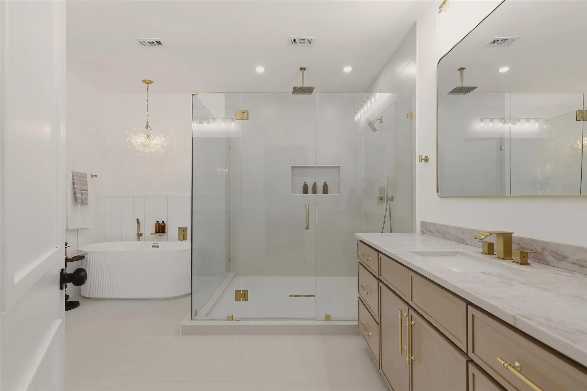Freestanding soaking tub, frameless glass shower enclosure with dual showerheads, dual vanity with undermount sinks, stone countertop, and gold-finish hardware throughout