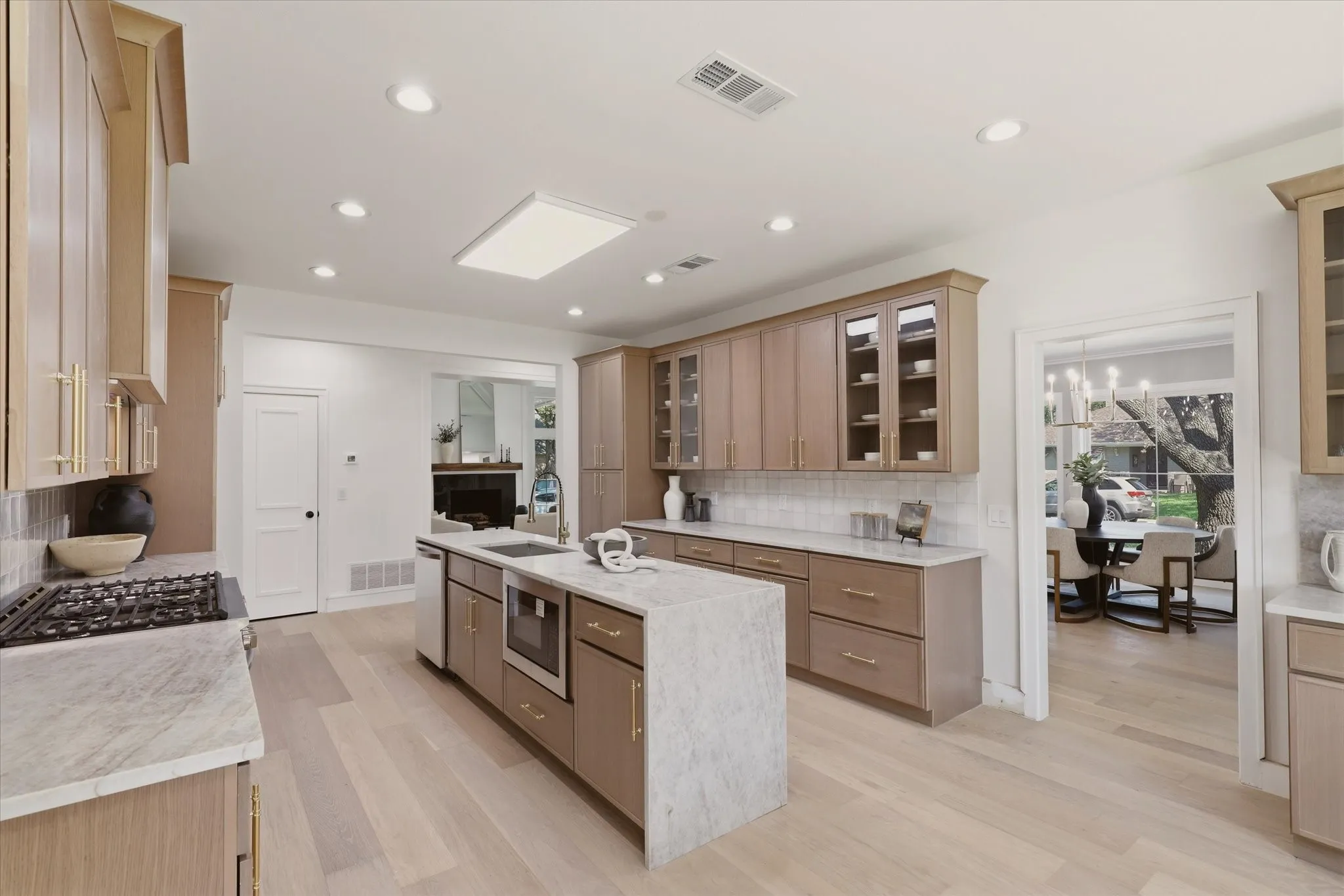 Kitchen featuring light wood-finish flooring, a large center island with integrated sink, stone countertops, and recessed lighting