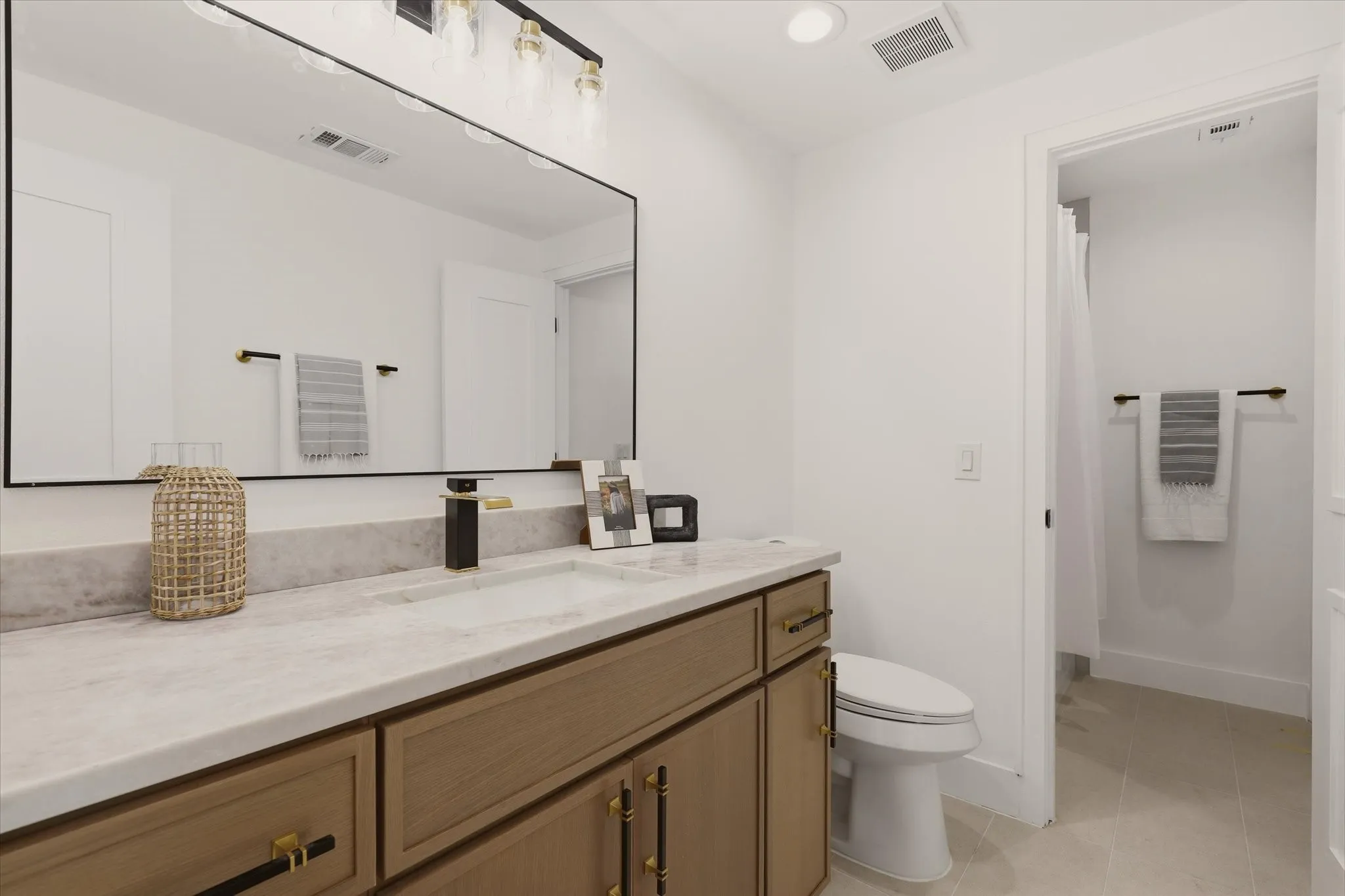 Light-finish wood vanity with gold hardware, a rectangular undermount sink, and a stone-finish countertop