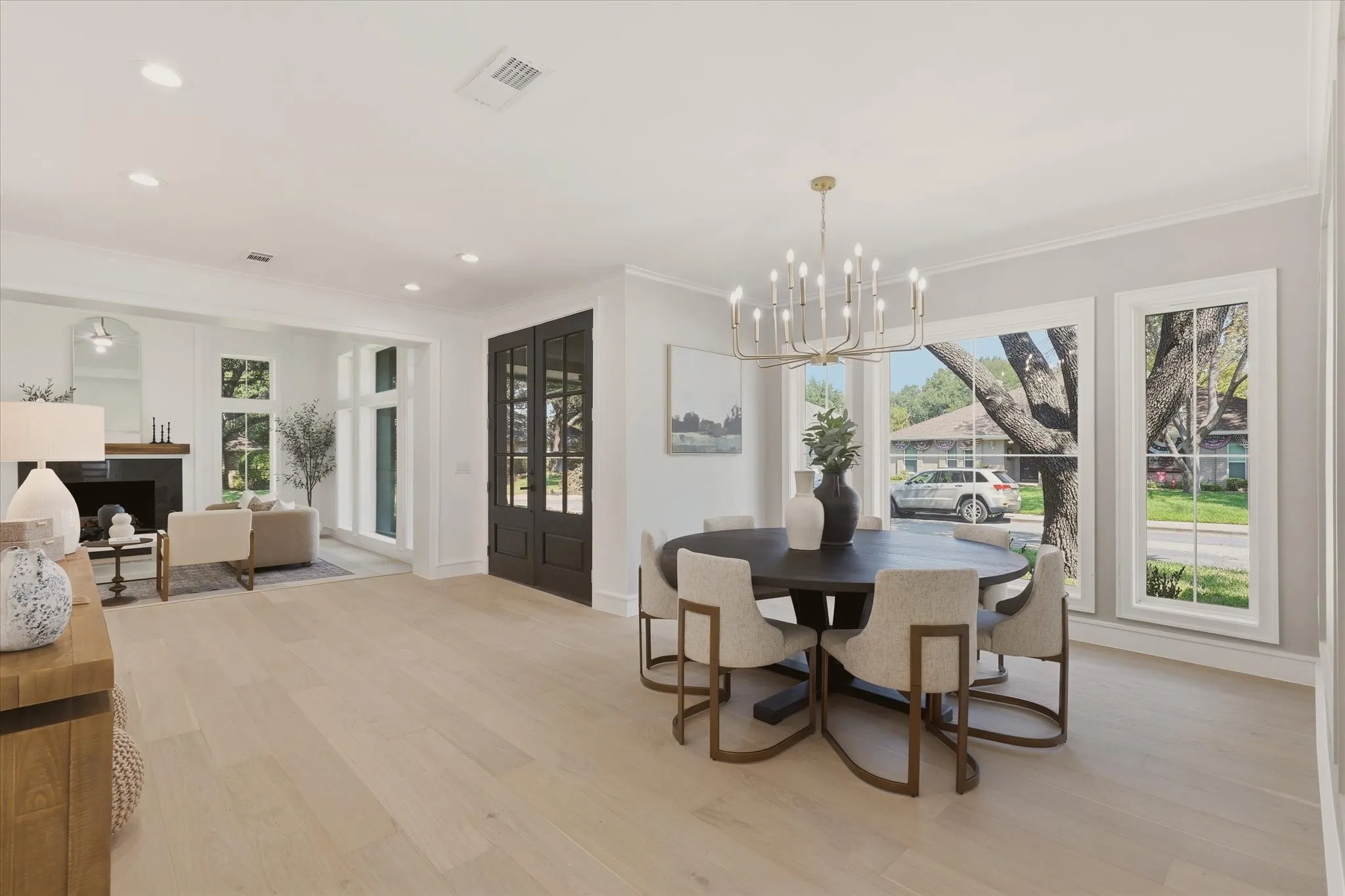 Expansive room featuring wood-finish flooring, recessed lighting, a fireplace with a dark mantel, multiple large windows, and a chandelier