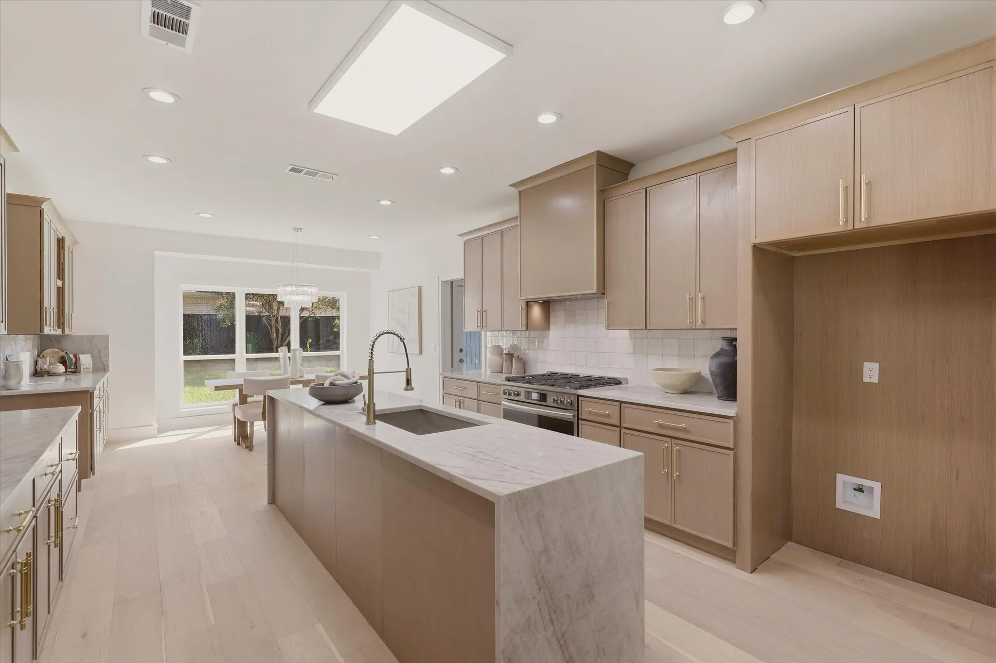 Integrated kitchen with a central island featuring a sink and faucet, light wood-finish cabinetry, subway tile backsplash, and light wood-finish flooring