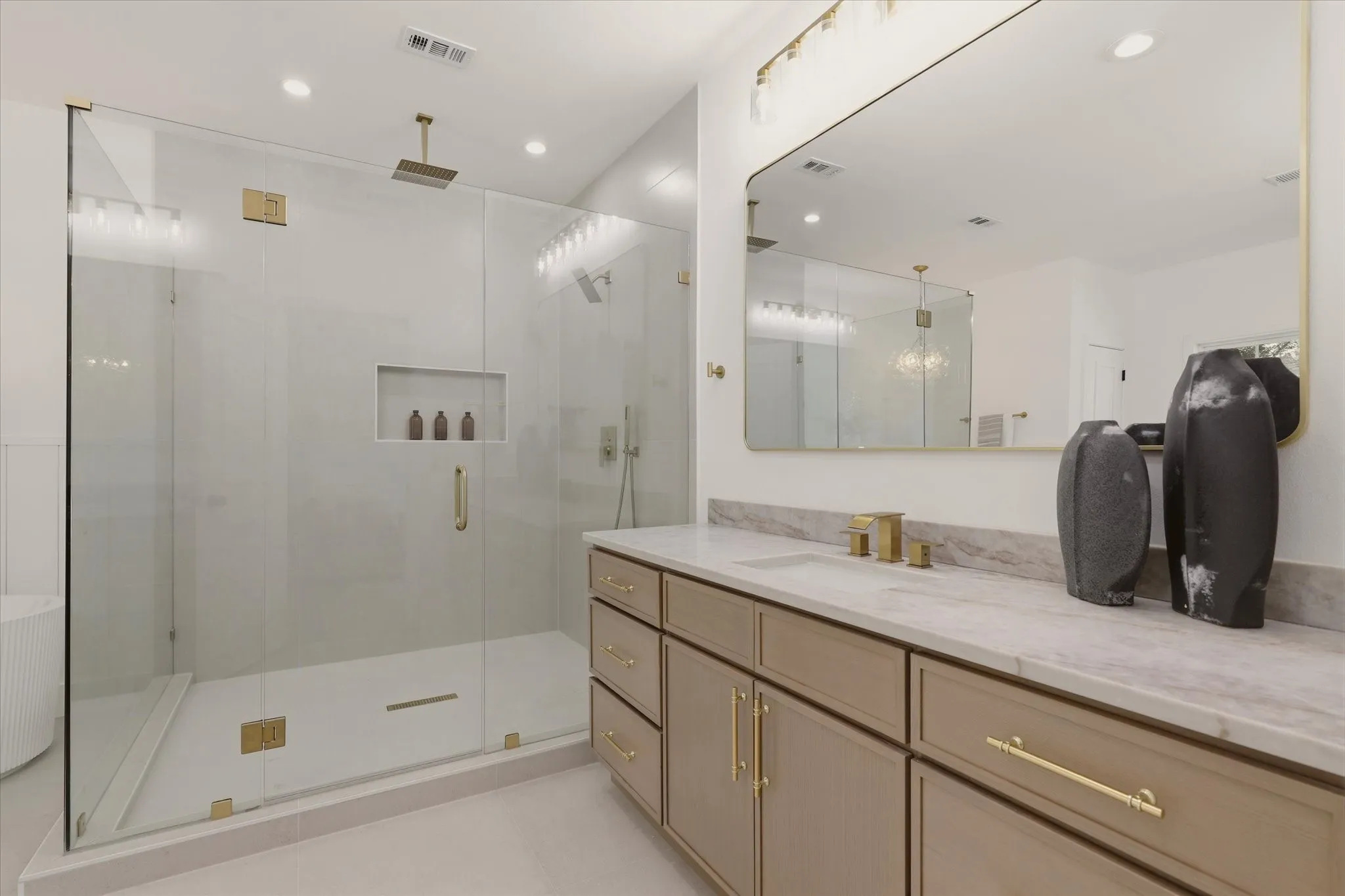 Expansive walk-in shower with a glass enclosure, built-in recessed shelf, and gold-finish fixtures