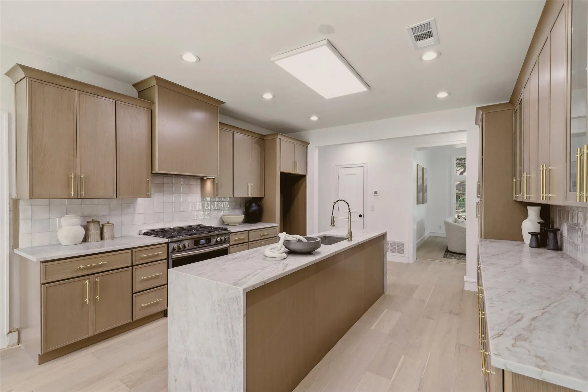 Gourmet kitchen with light wood-finish cabinetry, white tile backsplash, a center island featuring an undermount sink, and stainless steel appliances