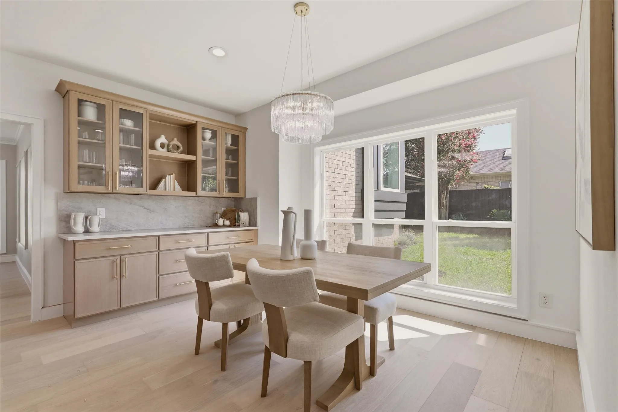 Light wood-finish flooring, built-in cabinetry with glass display doors, large picture window, recessed lighting, and a tiered chandelier