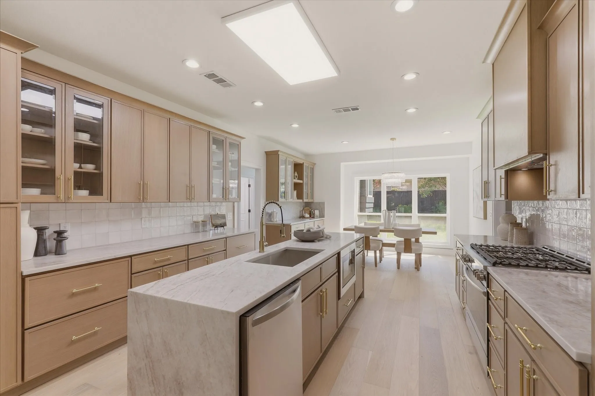 Gourmet kitchen with light wood-finish cabinetry, stone countertops, stainless steel appliances, and a central island with an undermount sink