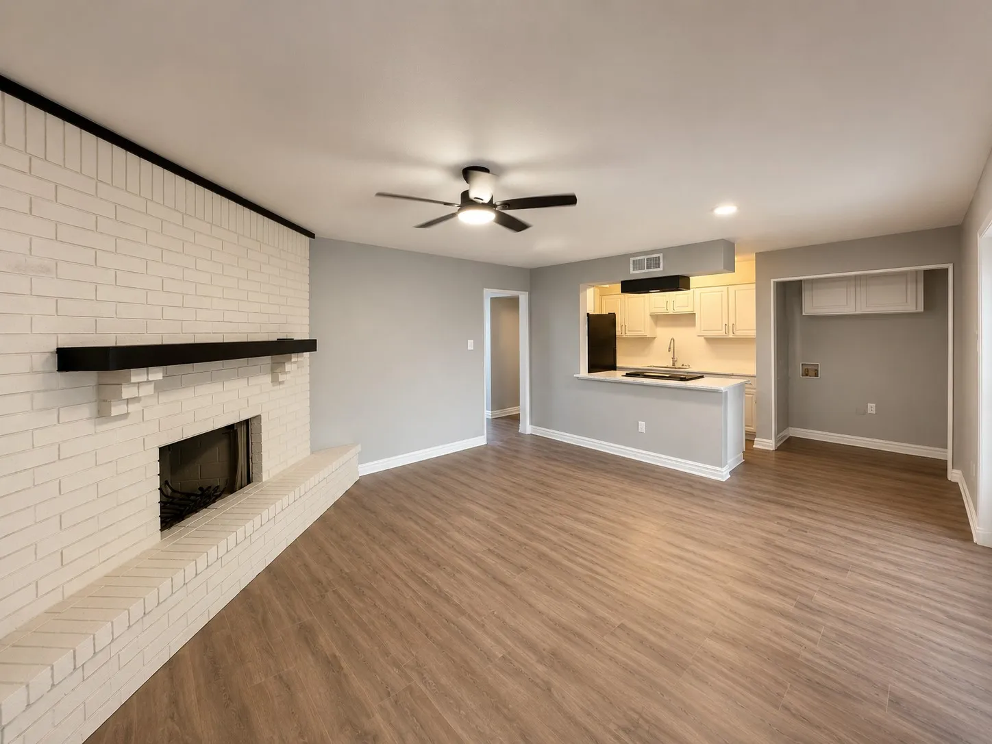White brick fireplace with a dark wood-finish mantel, wood-finish flooring, and recessed lighting