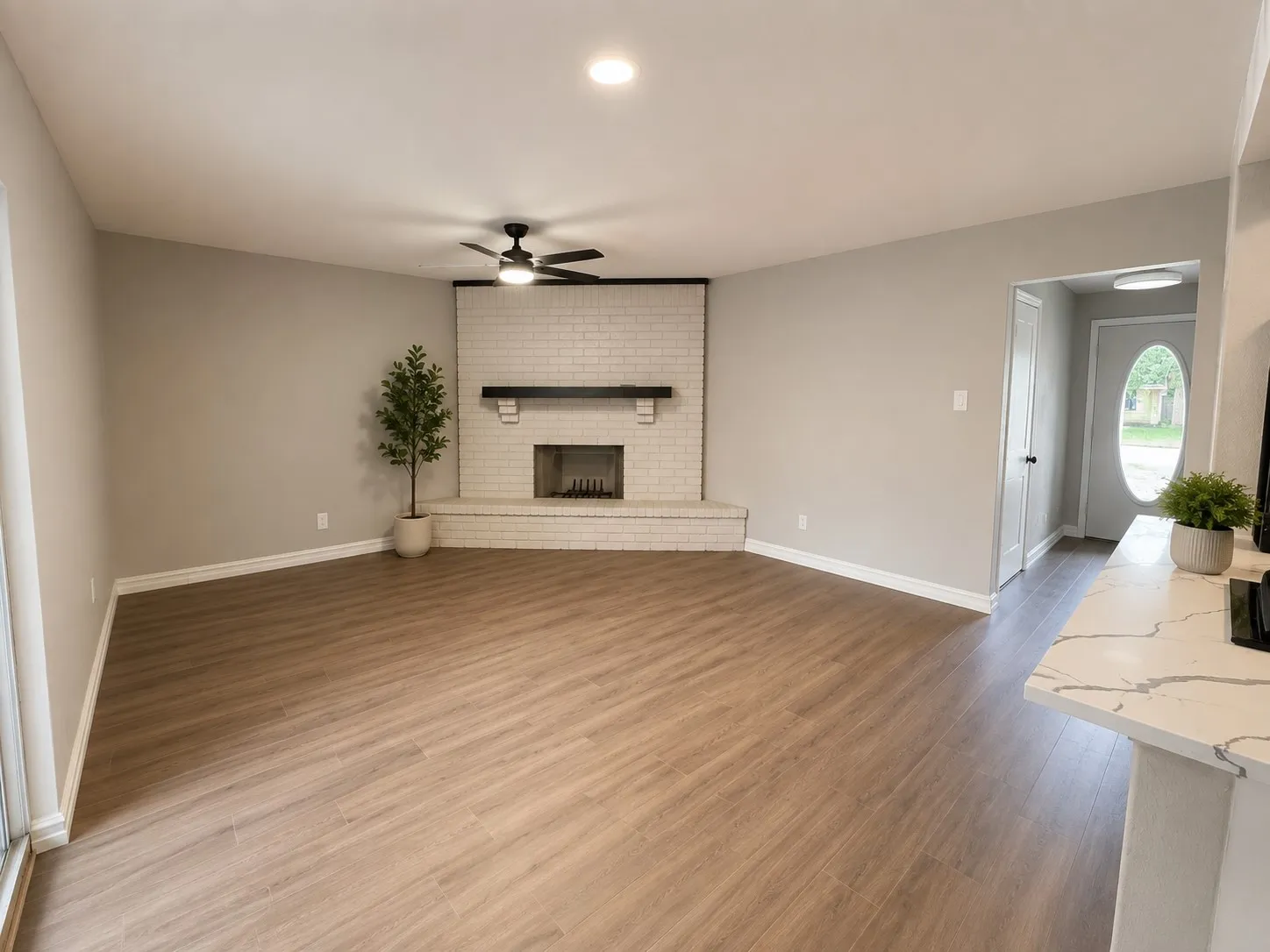 Wood-finish flooring throughout, white brick fireplace with dark wood mantel, recessed lighting, ceiling fan, and a white quartz-finish countertop