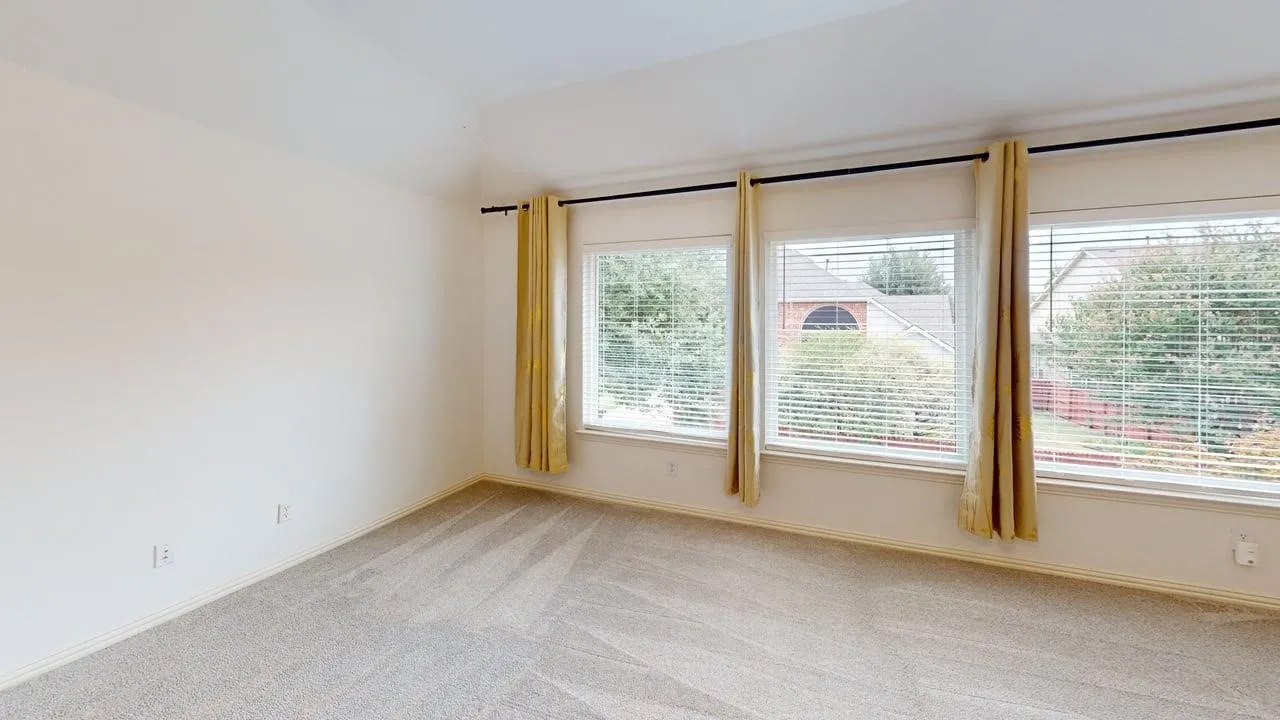 Vaulted ceiling with neutral carpeting and three expansive windows featuring blinds